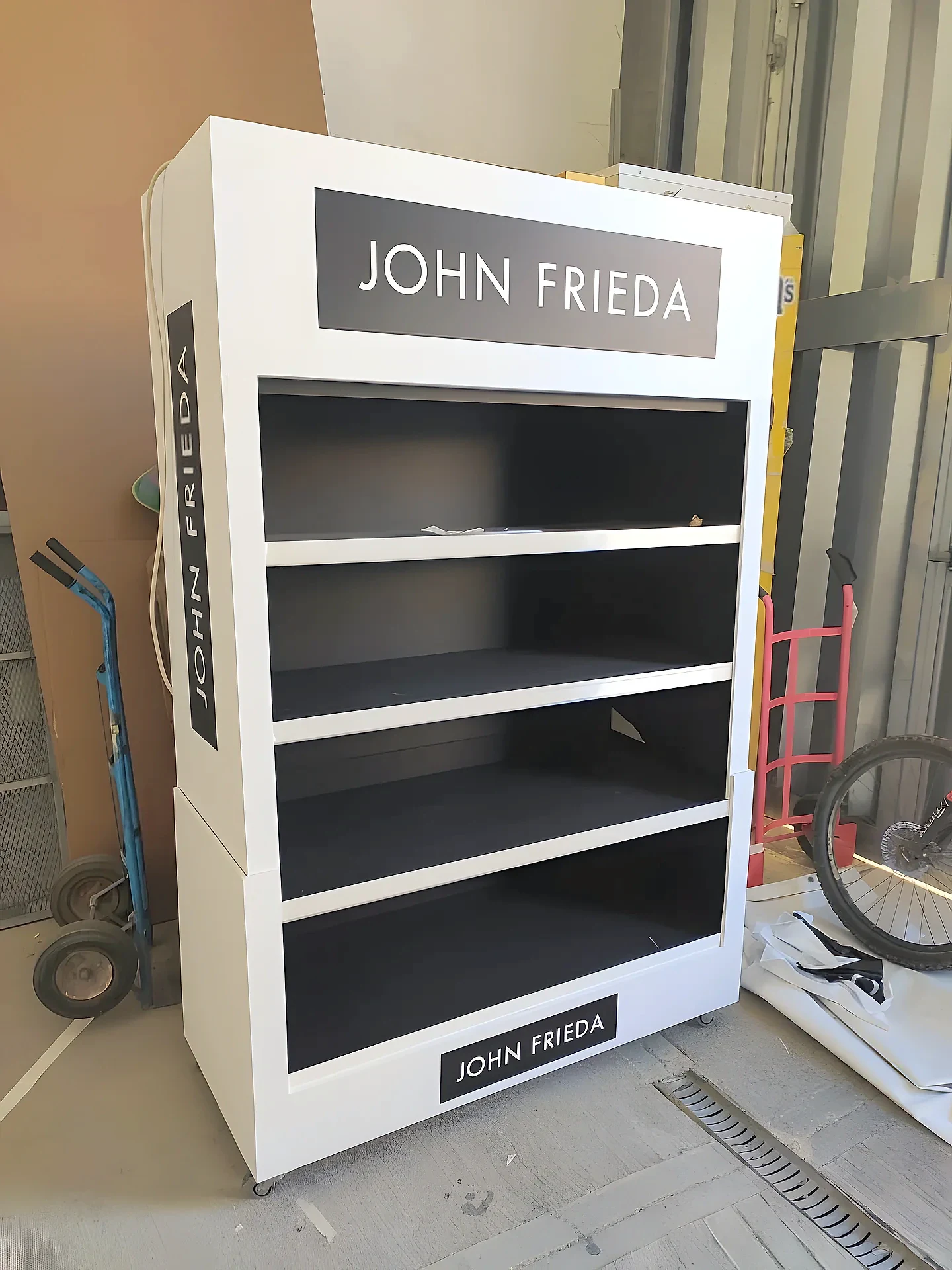 White four-shelf haircare display stand on castors with dark branded header and side panel
