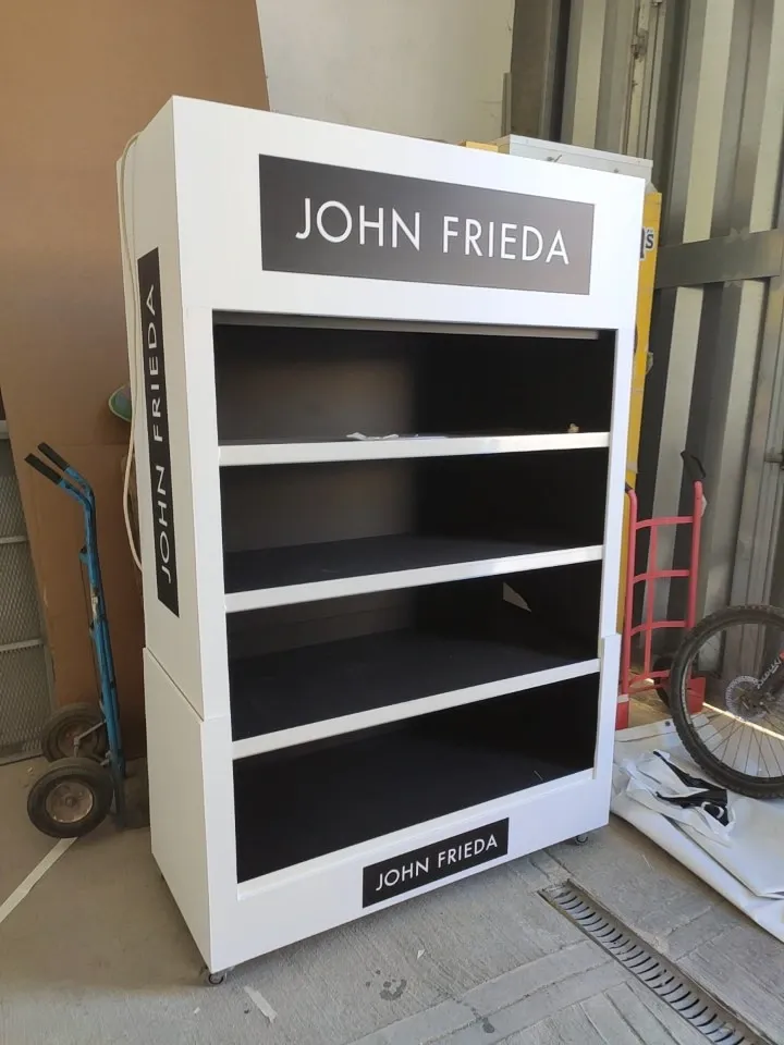 White four-shelf haircare display stand on castors with dark branded header and side panel