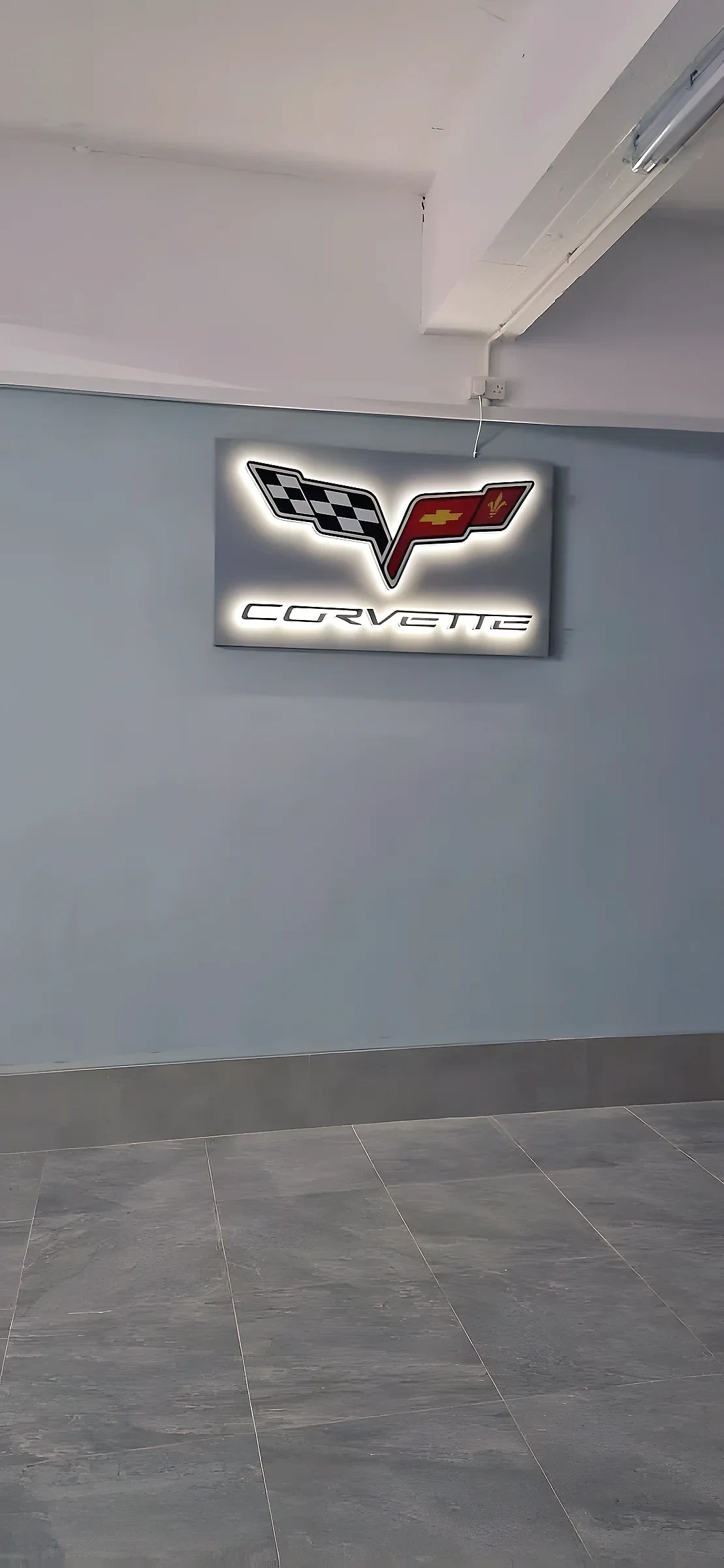Halo-lit car emblem panel glowing on a plain grey interior wall above a tiled floor
