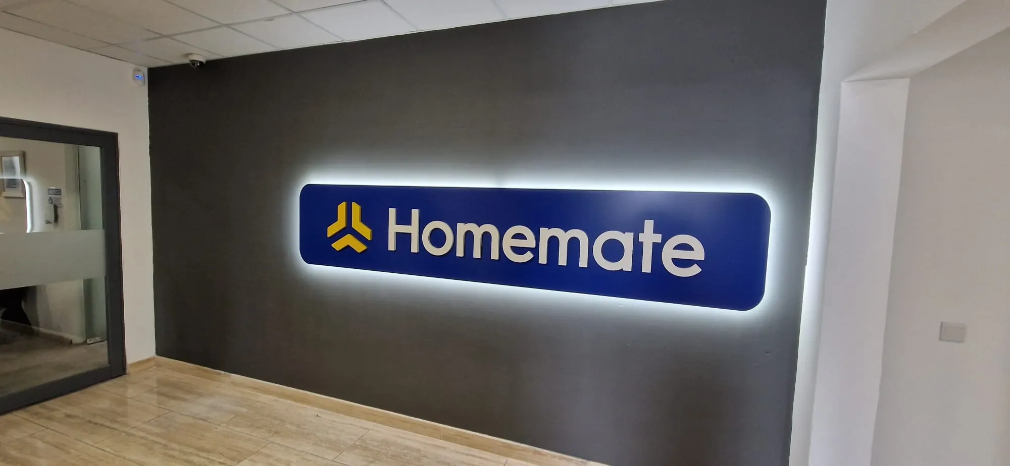 Blue halo-lit logo panel glowing against a dark grey reception wall above a wooden floor