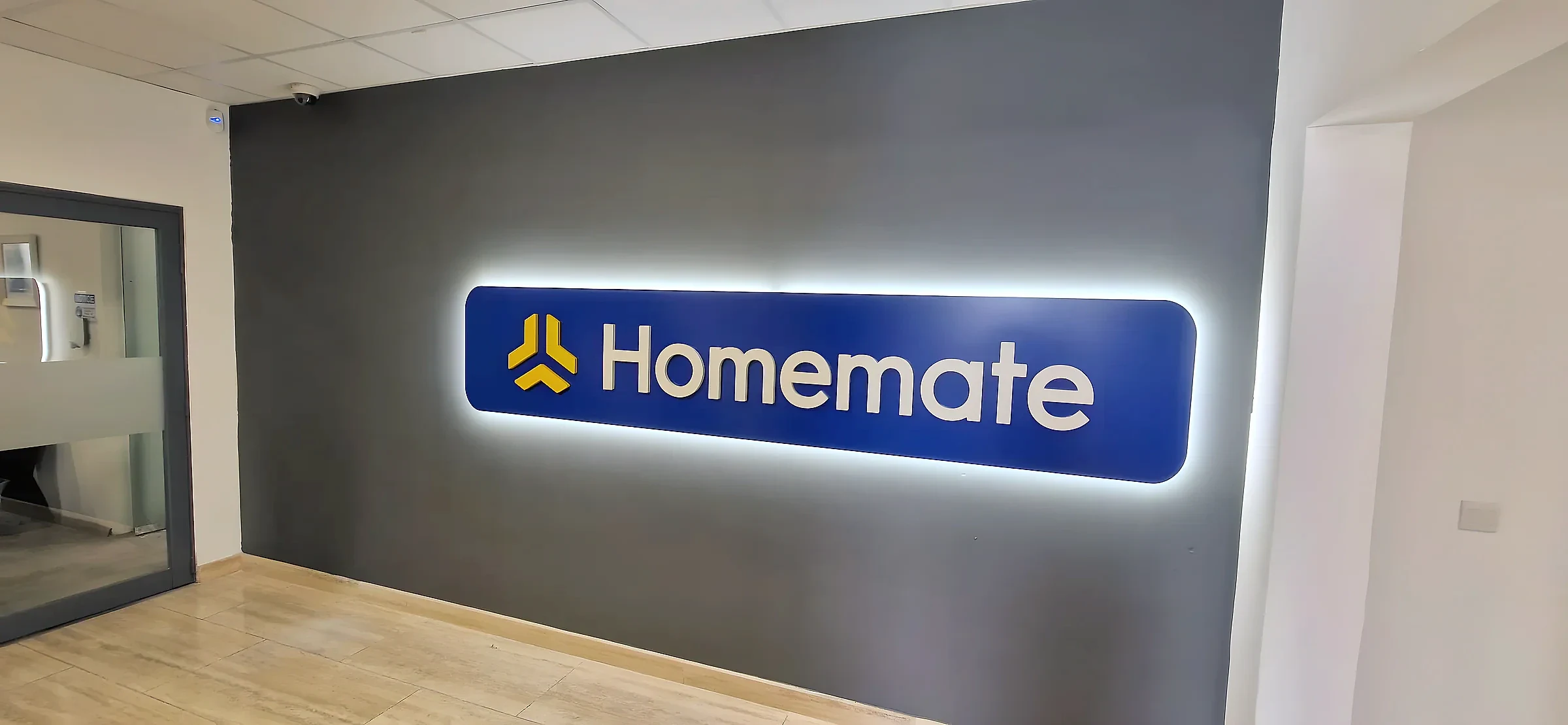 Blue halo-lit logo panel glowing against a dark grey reception wall above a wooden floor