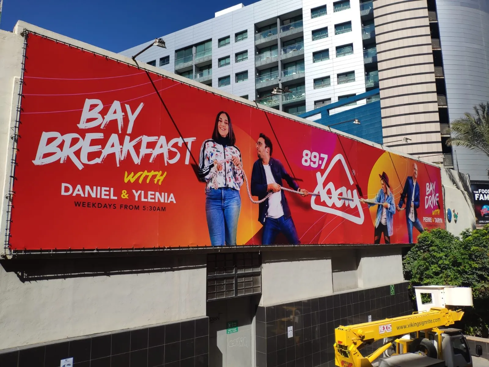 Large red printed banner with photographic figures mounted high on a hotel elevation
