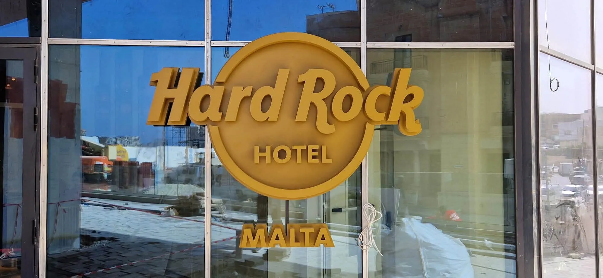 Circular hotel logo in gold applied to the ground-floor glazing, photographed from outside with the site still under construction