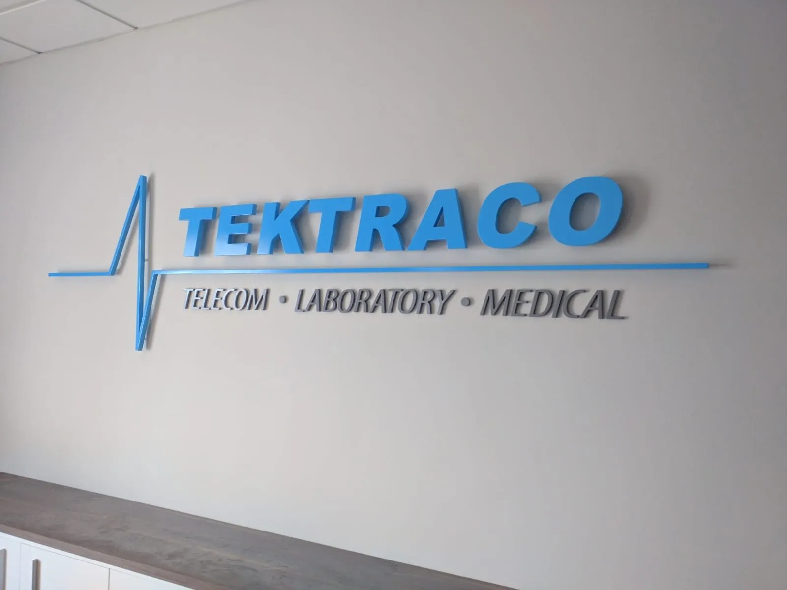 Blue illuminated three-dimensional lettering on a white wall above a thin divisional line of text