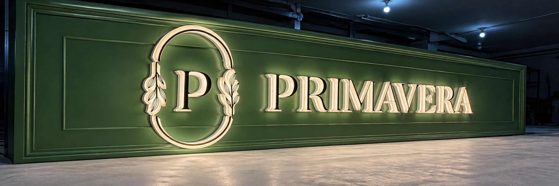Cream built-up letters and a leaf-framed emblem lit against a dark green panelled wall
