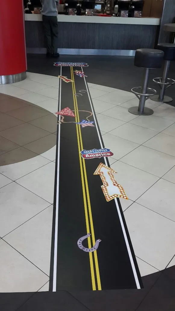 Printed road-marking floor graphic with yellow centre lines running across a tiled floor