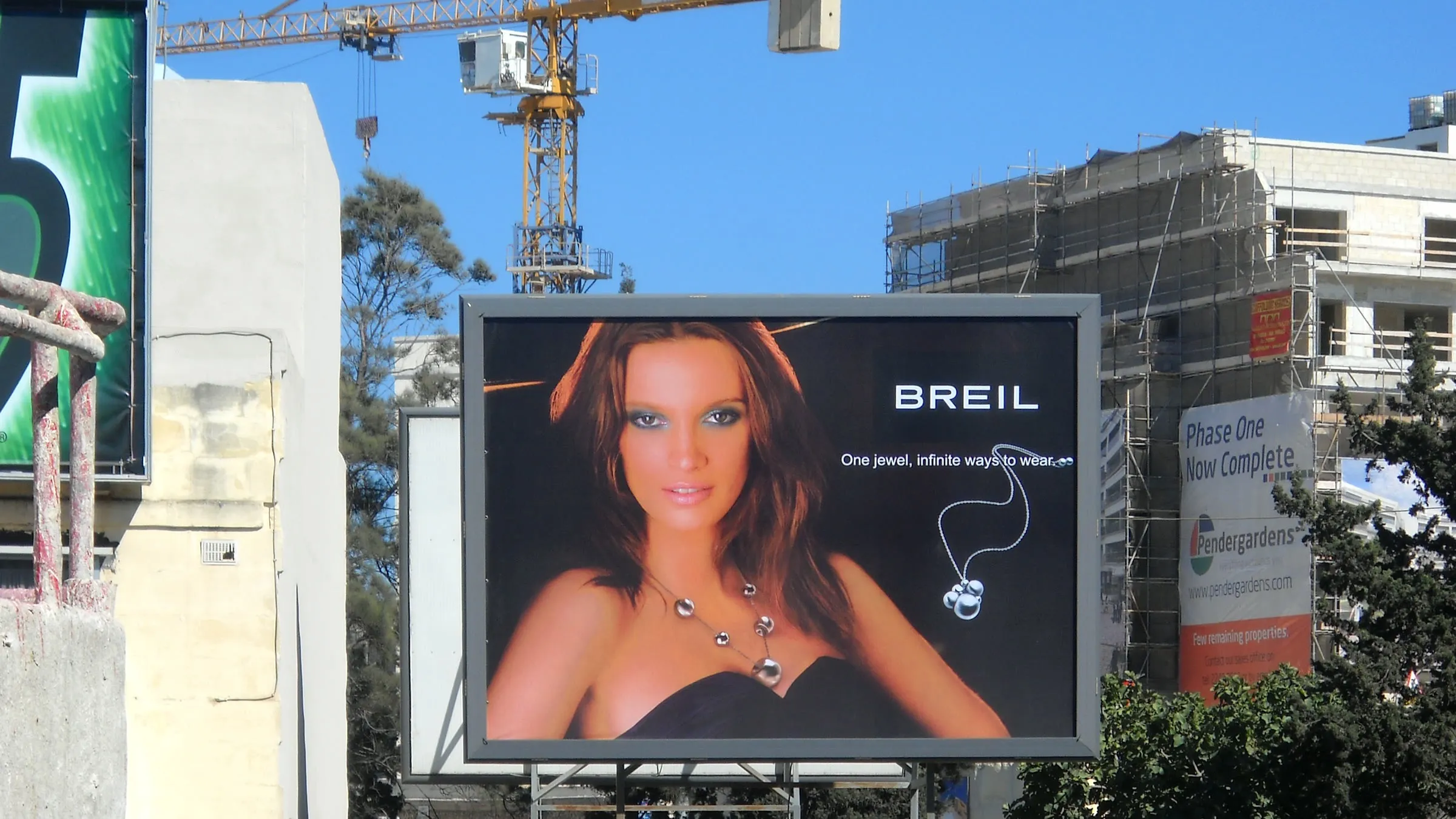 Roadside billboard mounted beside a construction site with a tower crane behind