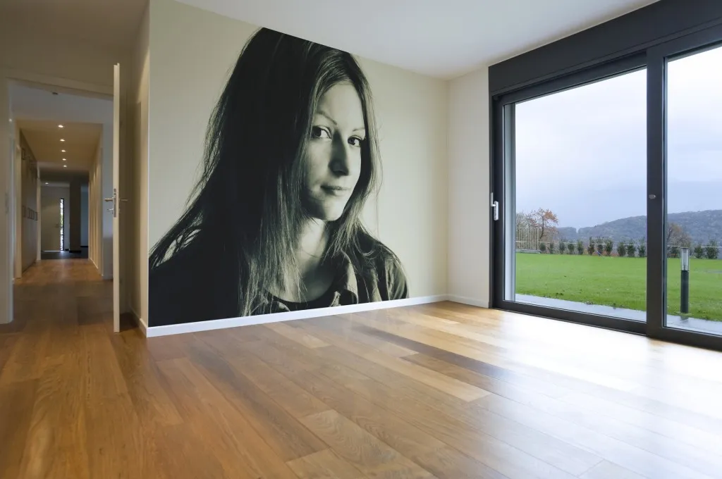 Large black-and-white portrait applied to the end wall of an empty room, running from the corner to the window reveal above a wood floor