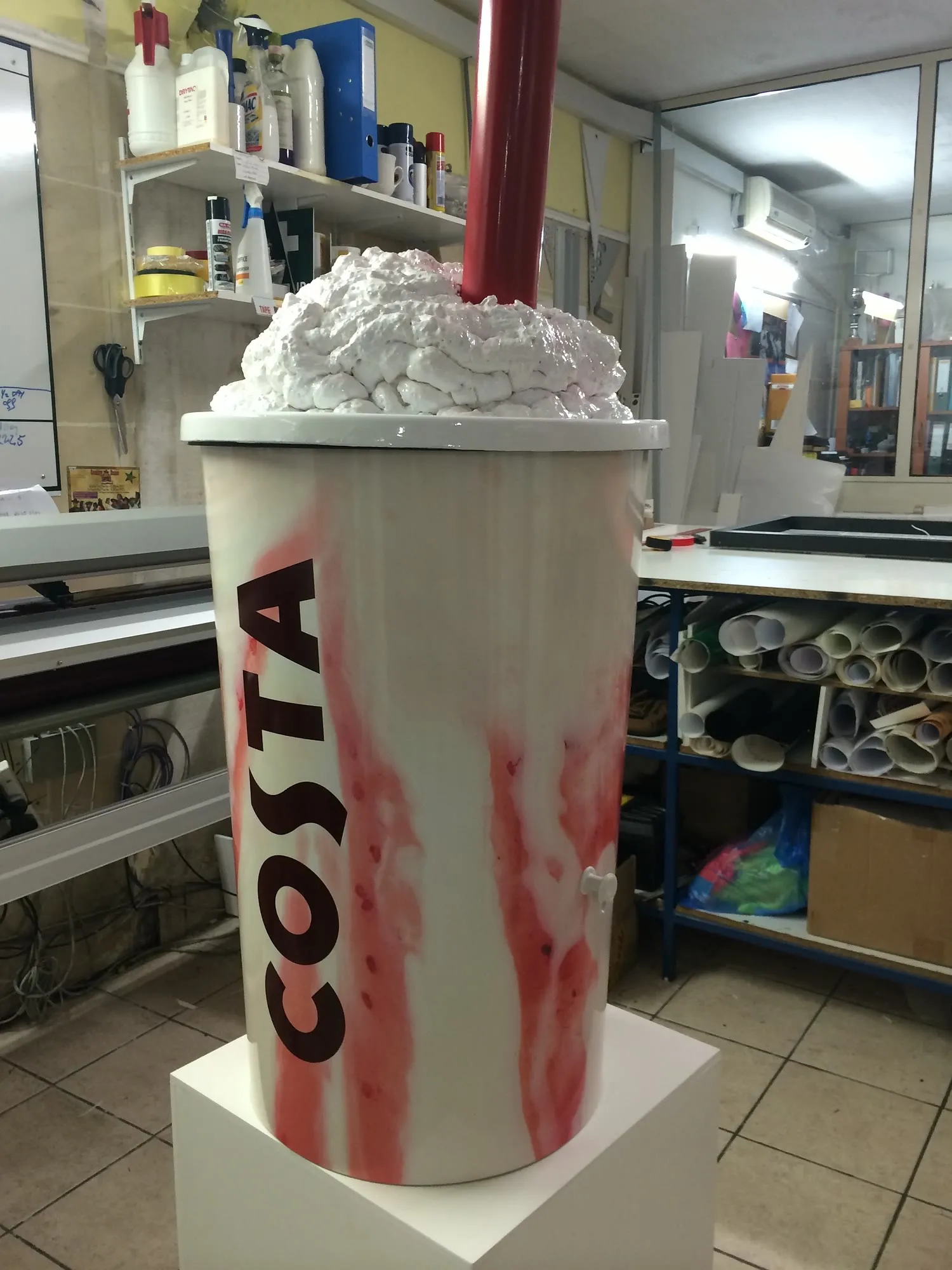 Tall oversized cup replica with lid standing in a production workshop
