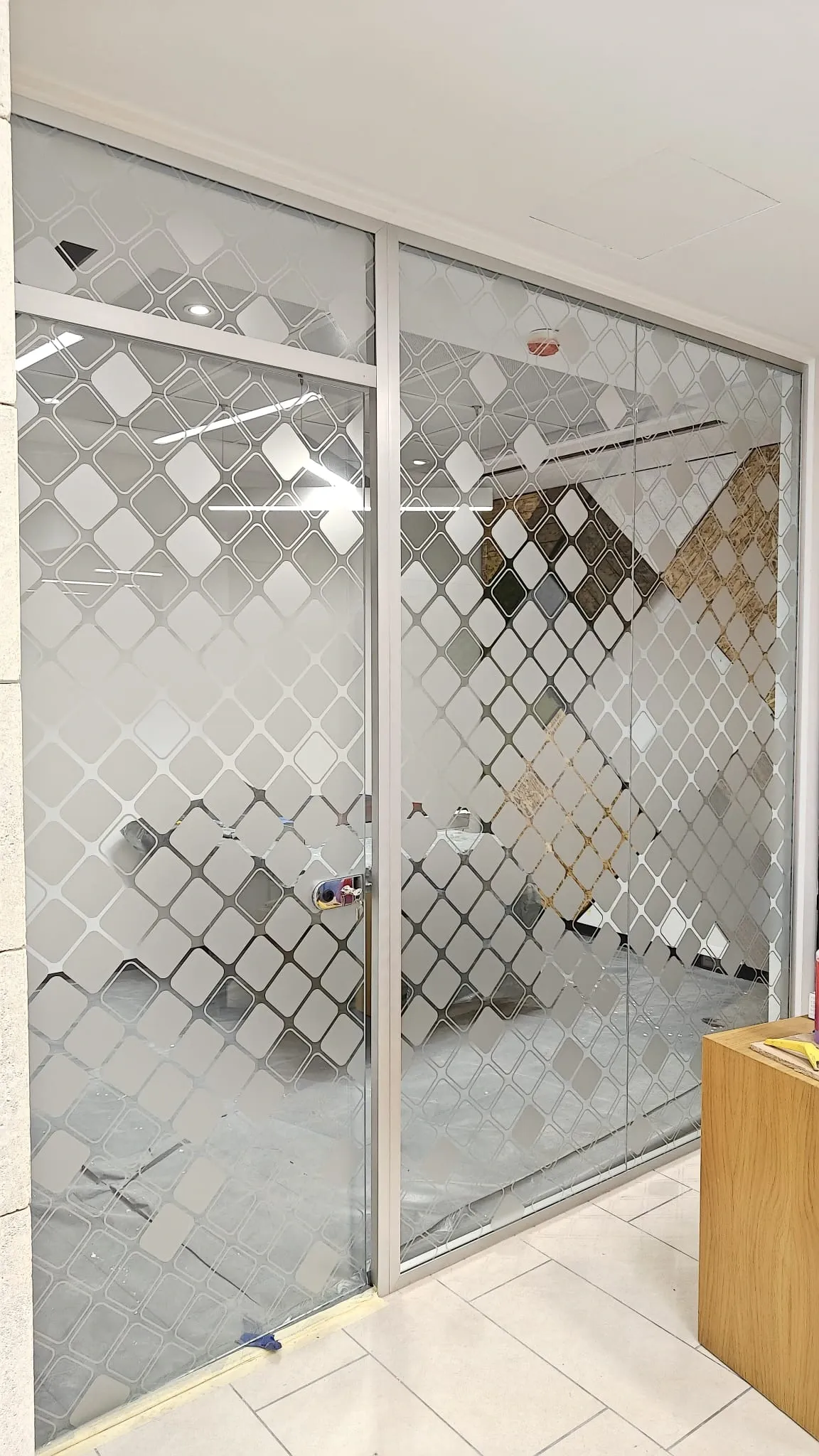 Full-height glass partition and sliding door covered in a frosted diamond lattice pattern