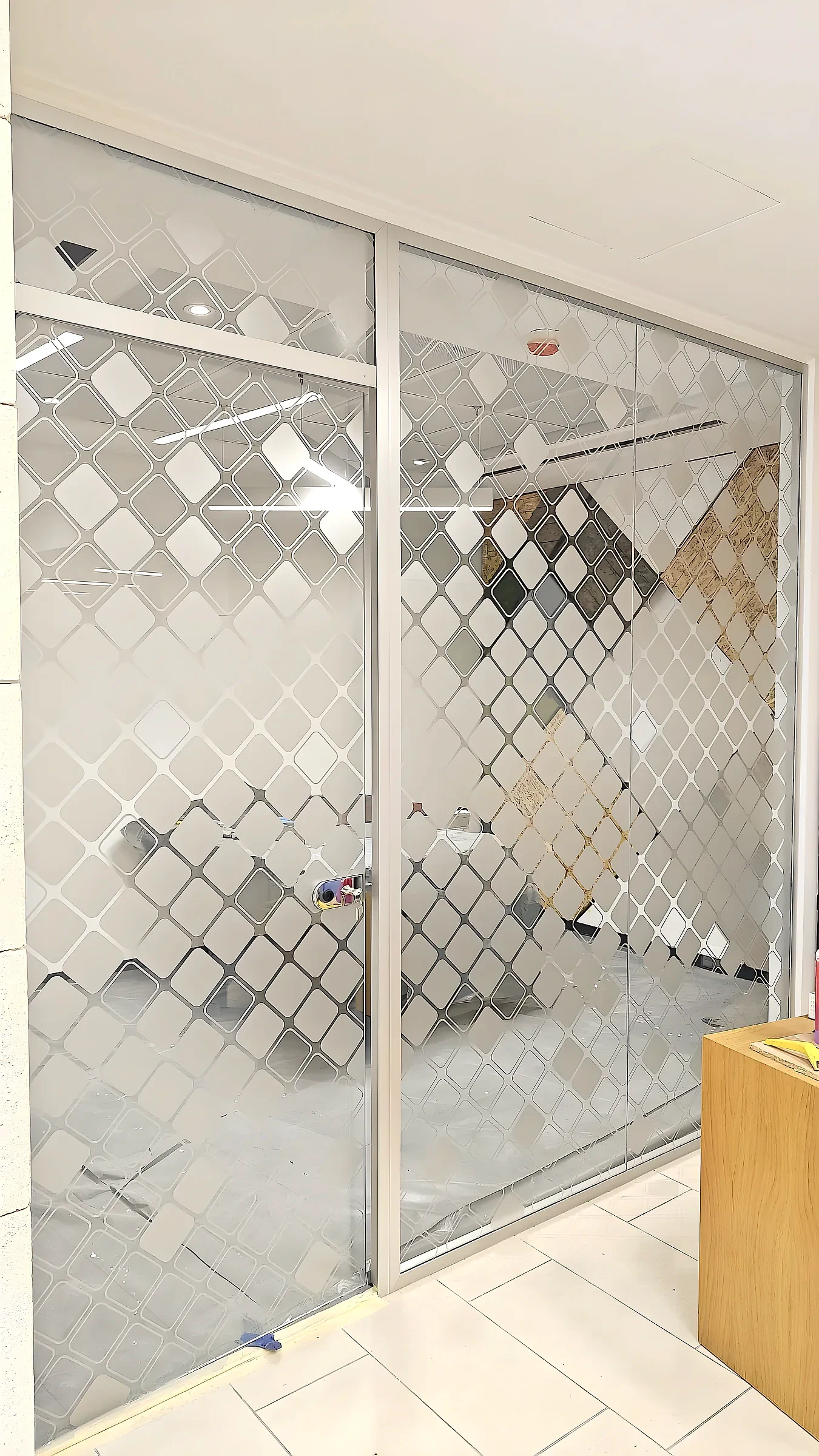 Full-height glass partition and sliding door covered in a frosted diamond lattice pattern