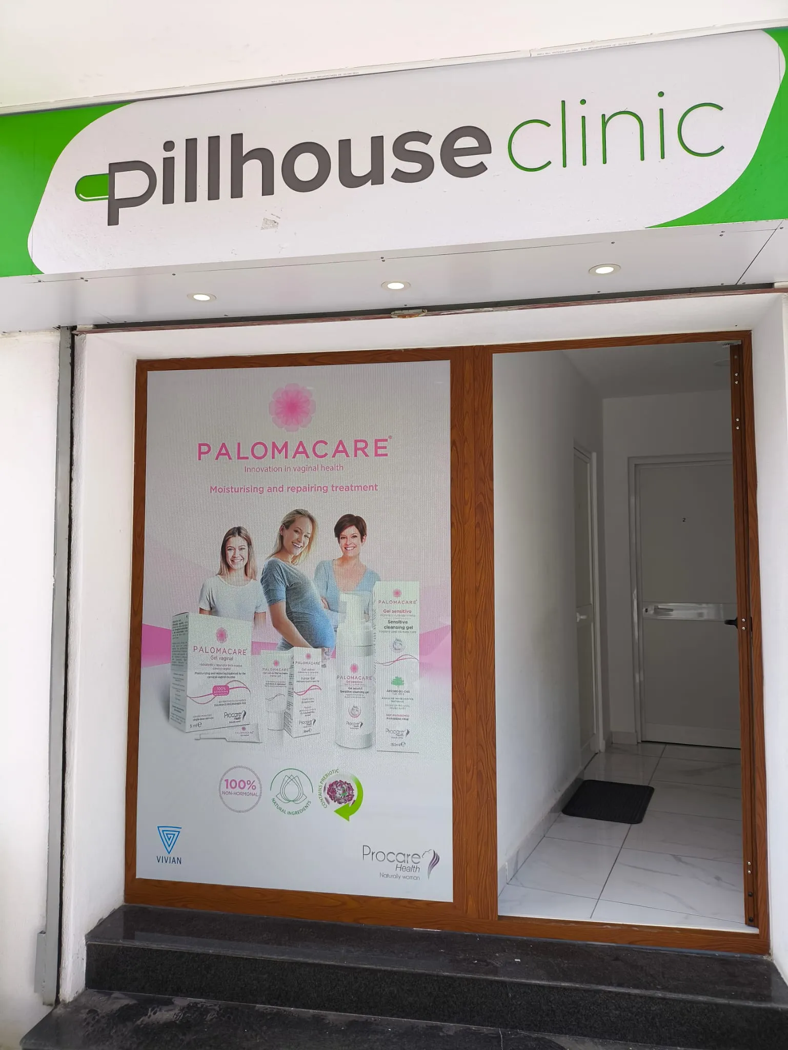 The same campaign panel fitted to a glazed clinic entrance beneath a green and white fascia sign