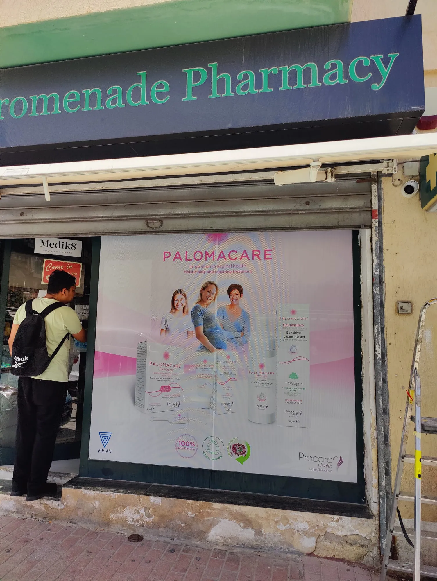 The same campaign panel fitted to a shopfront window beneath a painted fascia, with the shutter box above