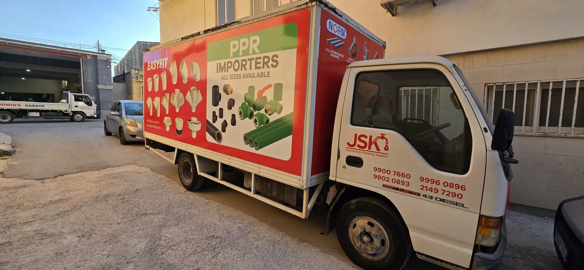 White box truck with a red and green printed panel of plumbing fittings along its body