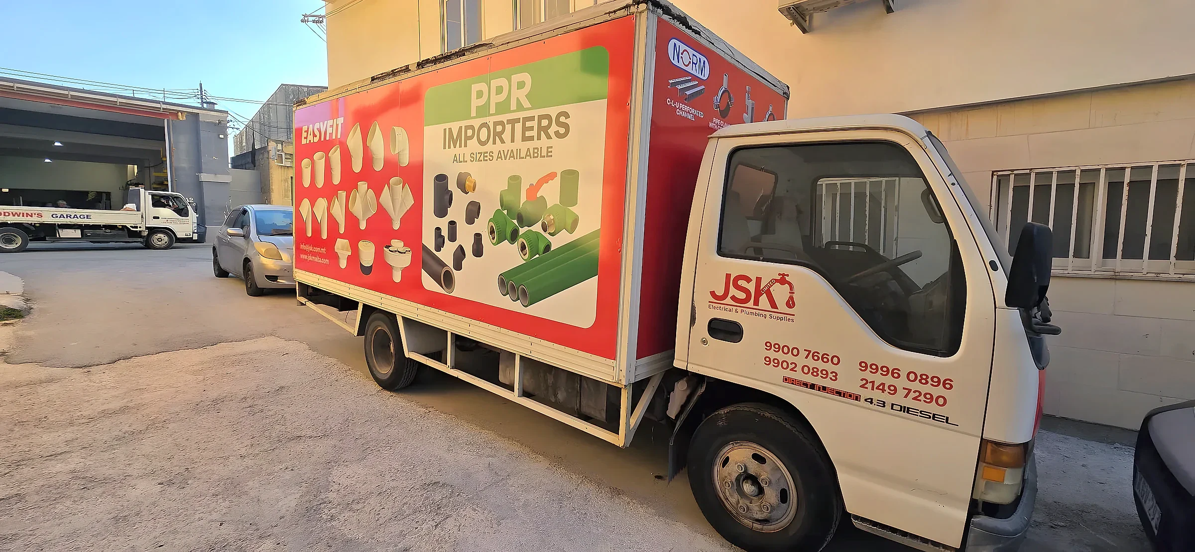 White box truck with a red and green printed panel of plumbing fittings along its body