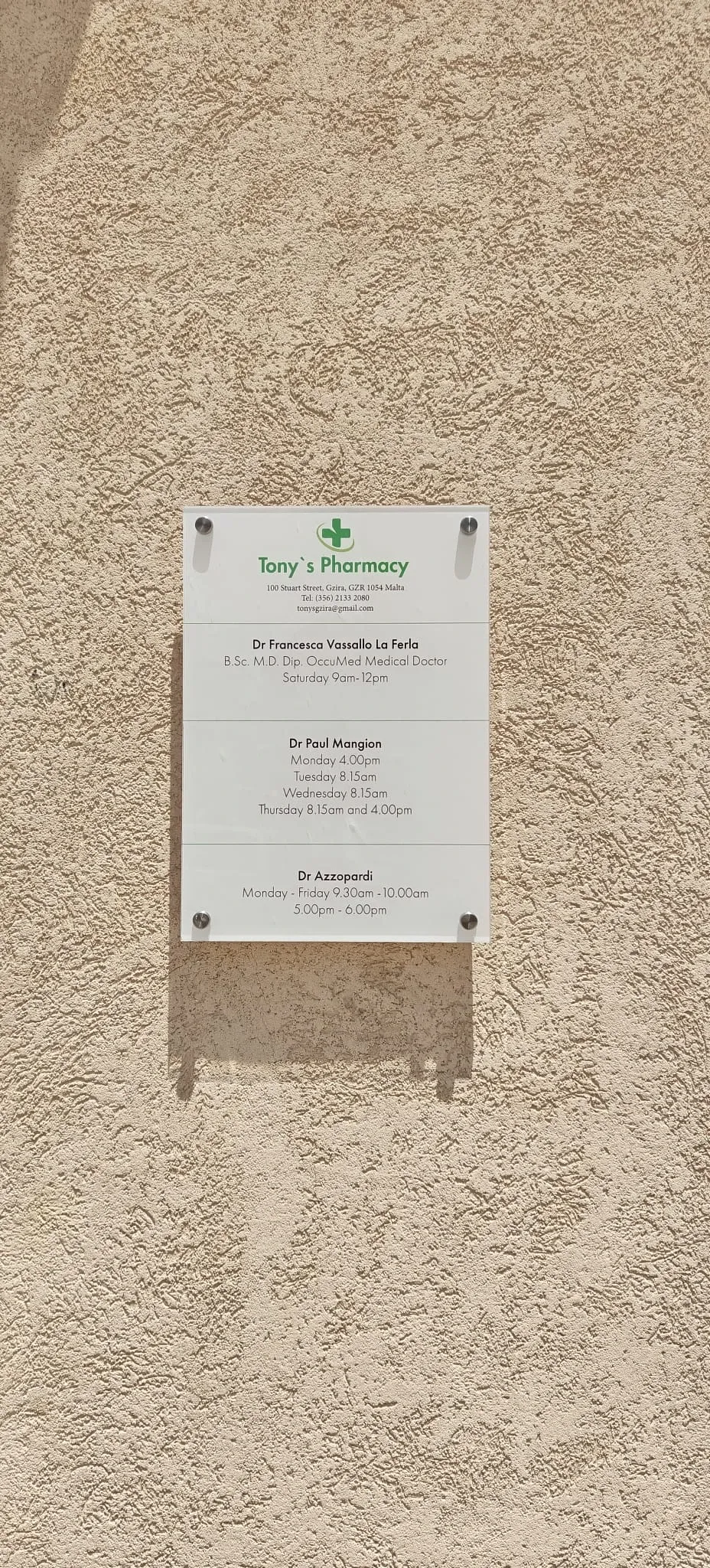 Clear acrylic plaque listing pharmacy consulting hours fixed to a stone wall on standoffs