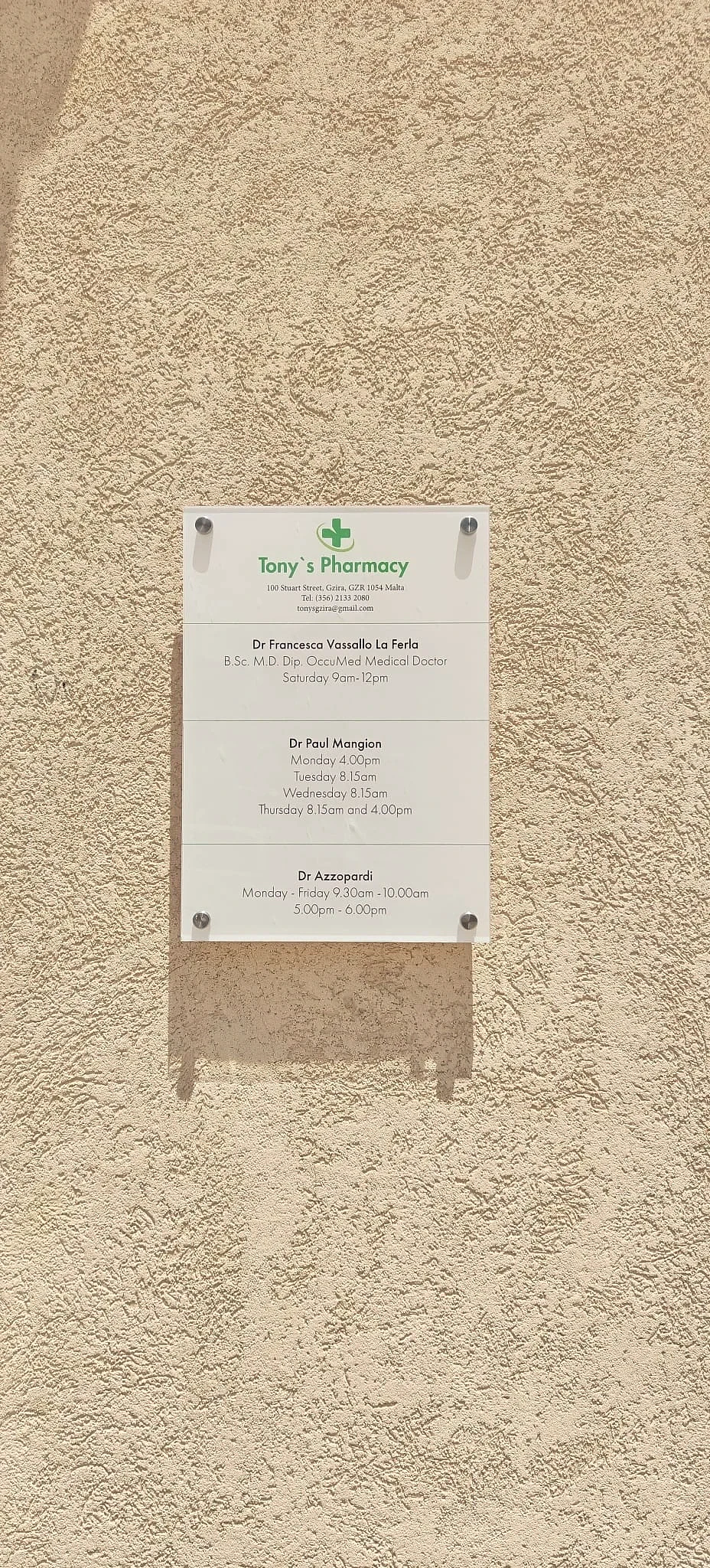 Clear acrylic plaque listing pharmacy consulting hours fixed to a stone wall on standoffs