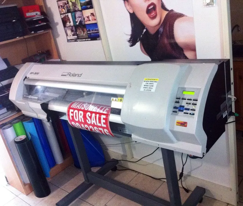 Print-and-cut plotter on a stand producing a red and white printed vinyl panel
