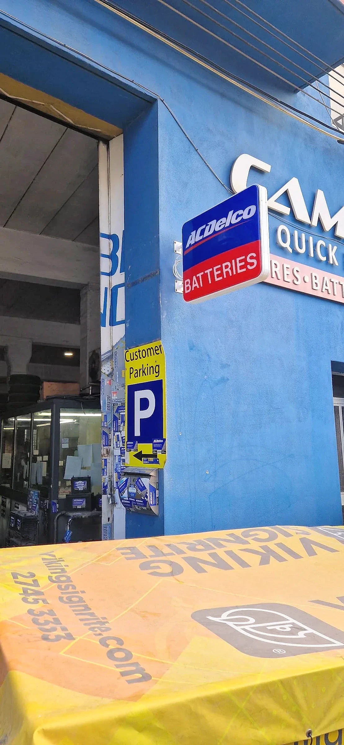 Blue projecting battery sign and a parking plate fitted to a blue workshop frontage above a covered bench