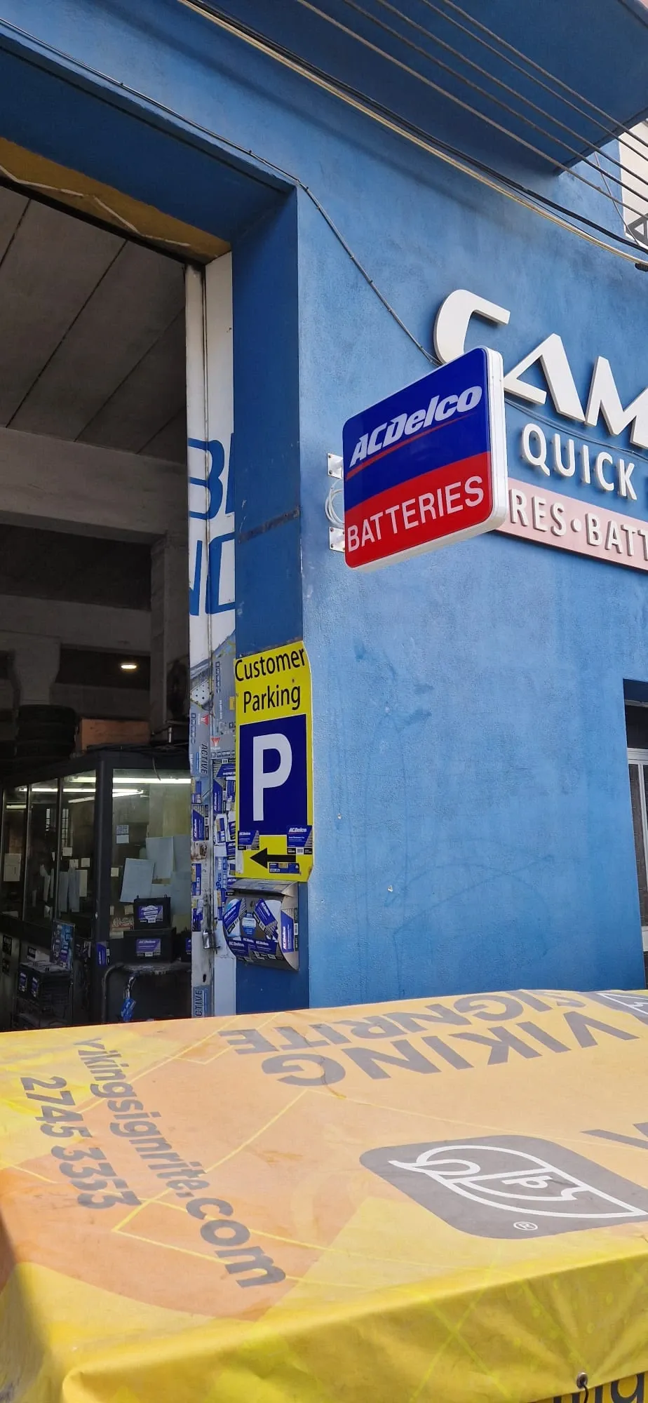 Blue projecting battery sign and a parking plate fitted to a blue workshop frontage above a covered bench