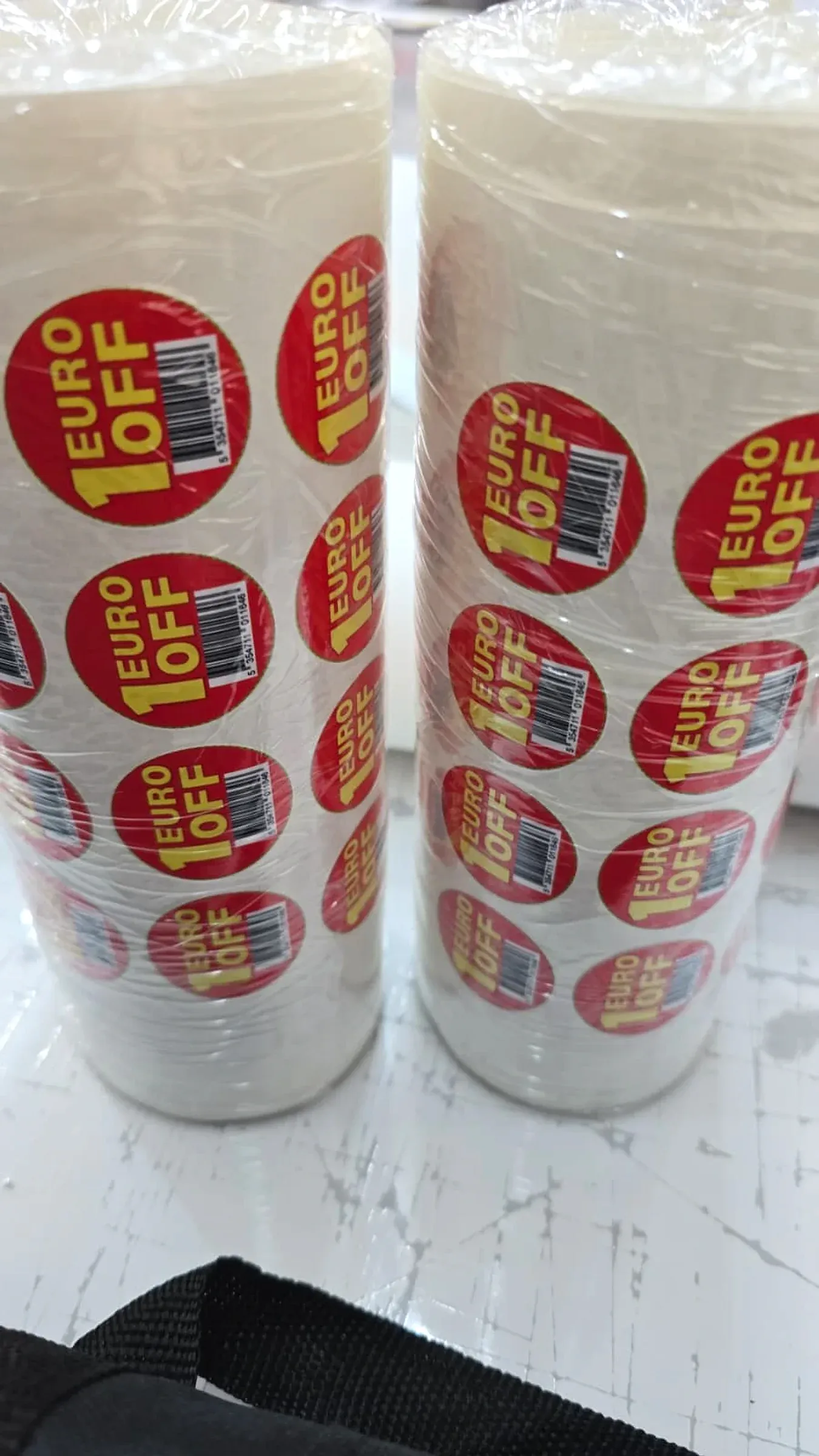 Two shrink-wrapped stacks of rolls of round red price-off labels on a workbench