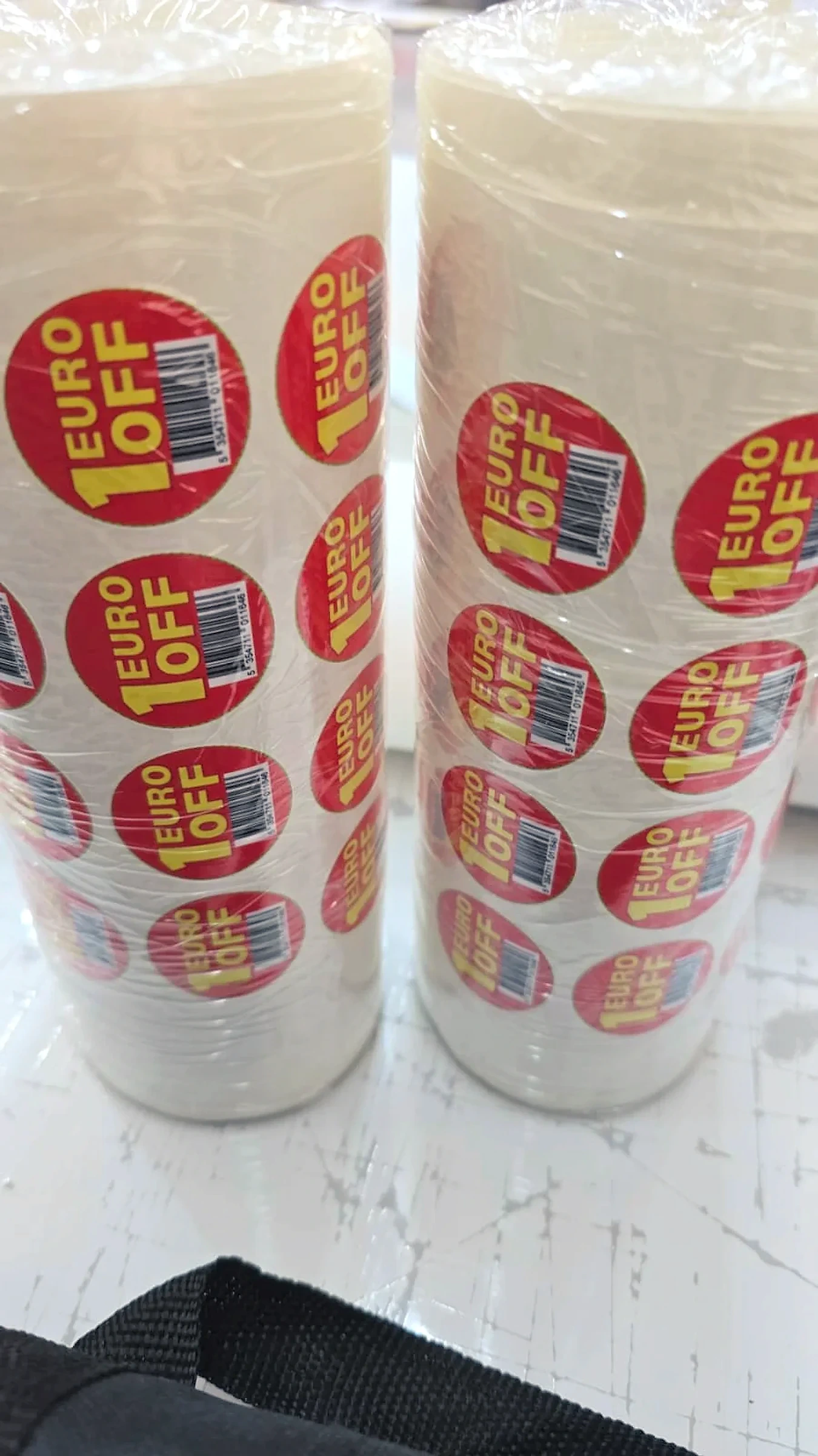 Two shrink-wrapped stacks of rolls of round red price-off labels on a workbench