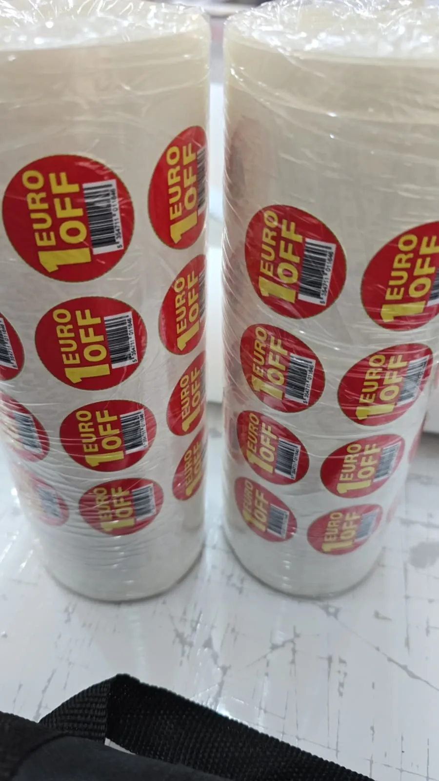 Two shrink-wrapped stacks of rolls of round red price-off labels on a workbench