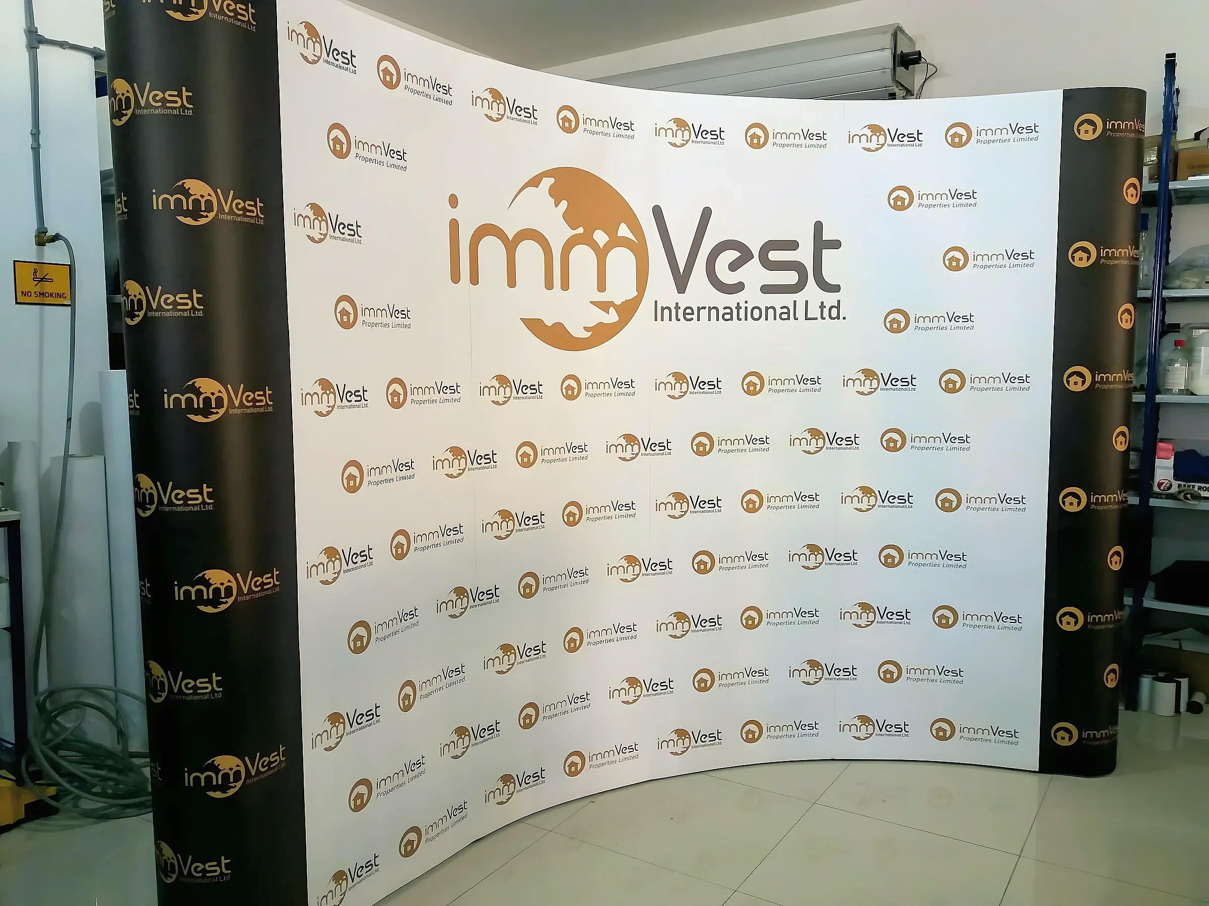 Curved fabric backdrop printed with a repeating property company logo, set up in a workshop