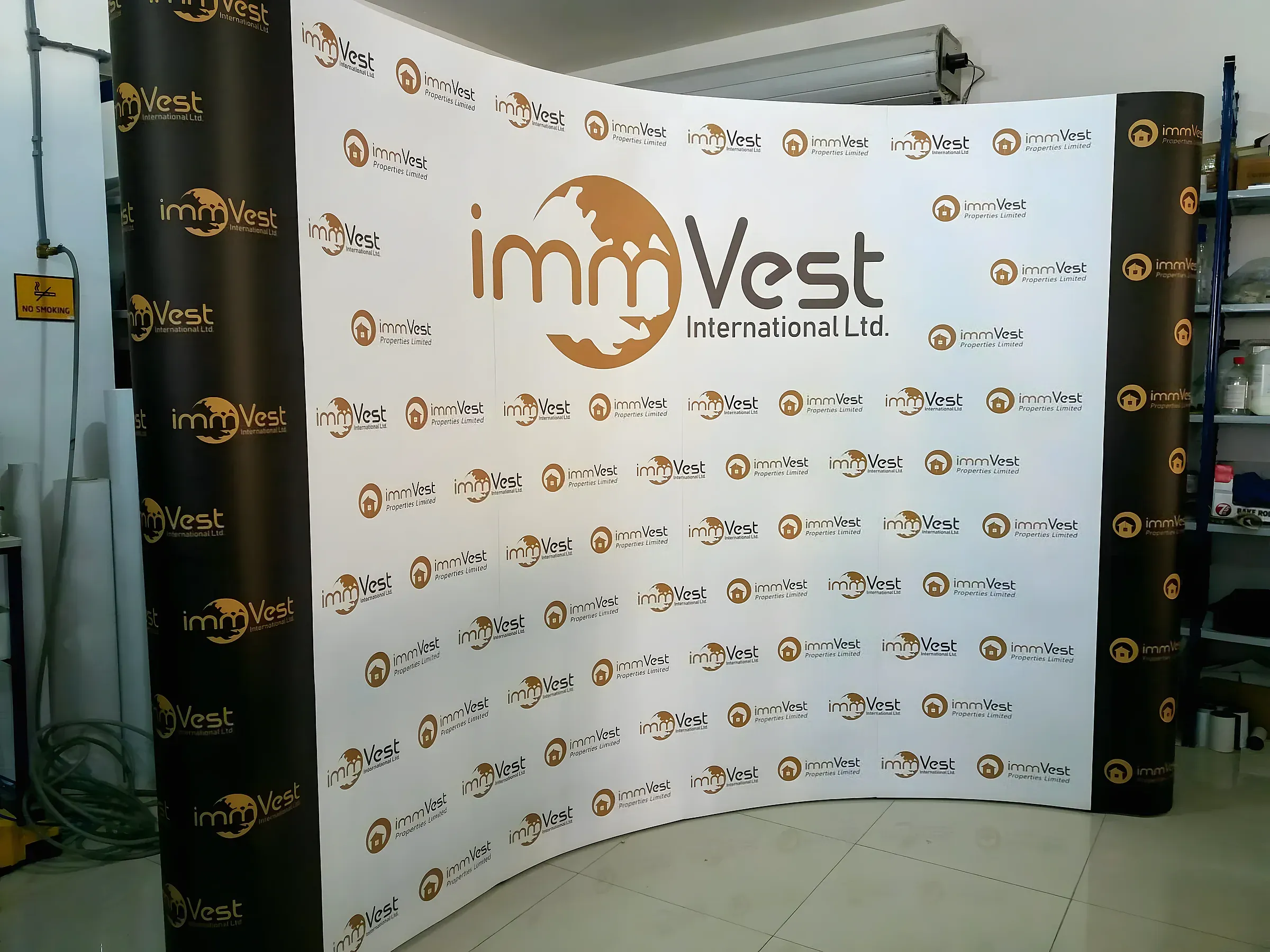 Curved fabric backdrop printed with a repeating property company logo, set up in a workshop