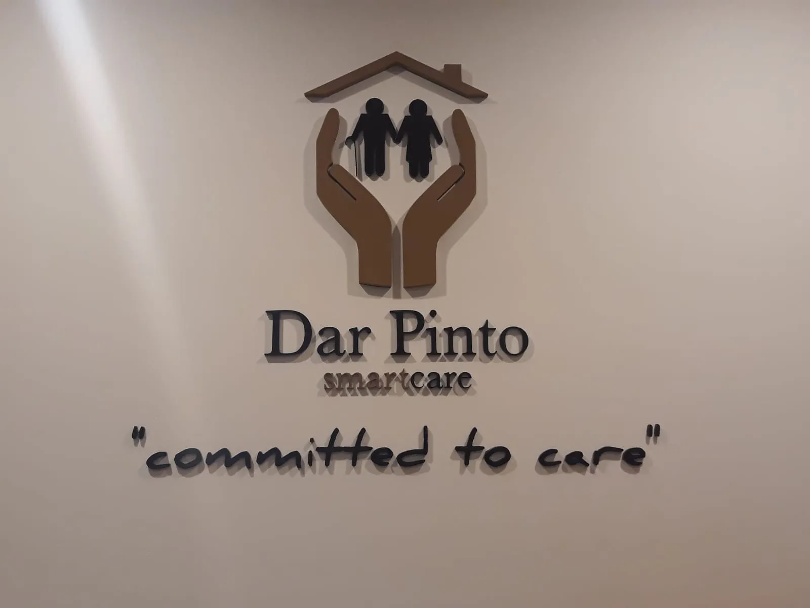 Brown raised lettering and a rounded logo mark on a pale reception wall above a painted strapline