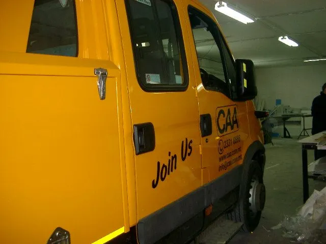 Yellow flatbed recovery truck with dark livery and contact details along the cab and bed