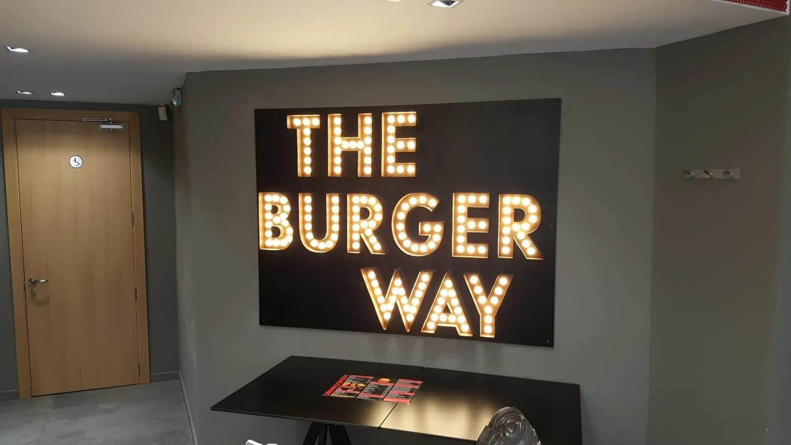 Large warm-white illuminated letters mounted on a dark grey interior wall