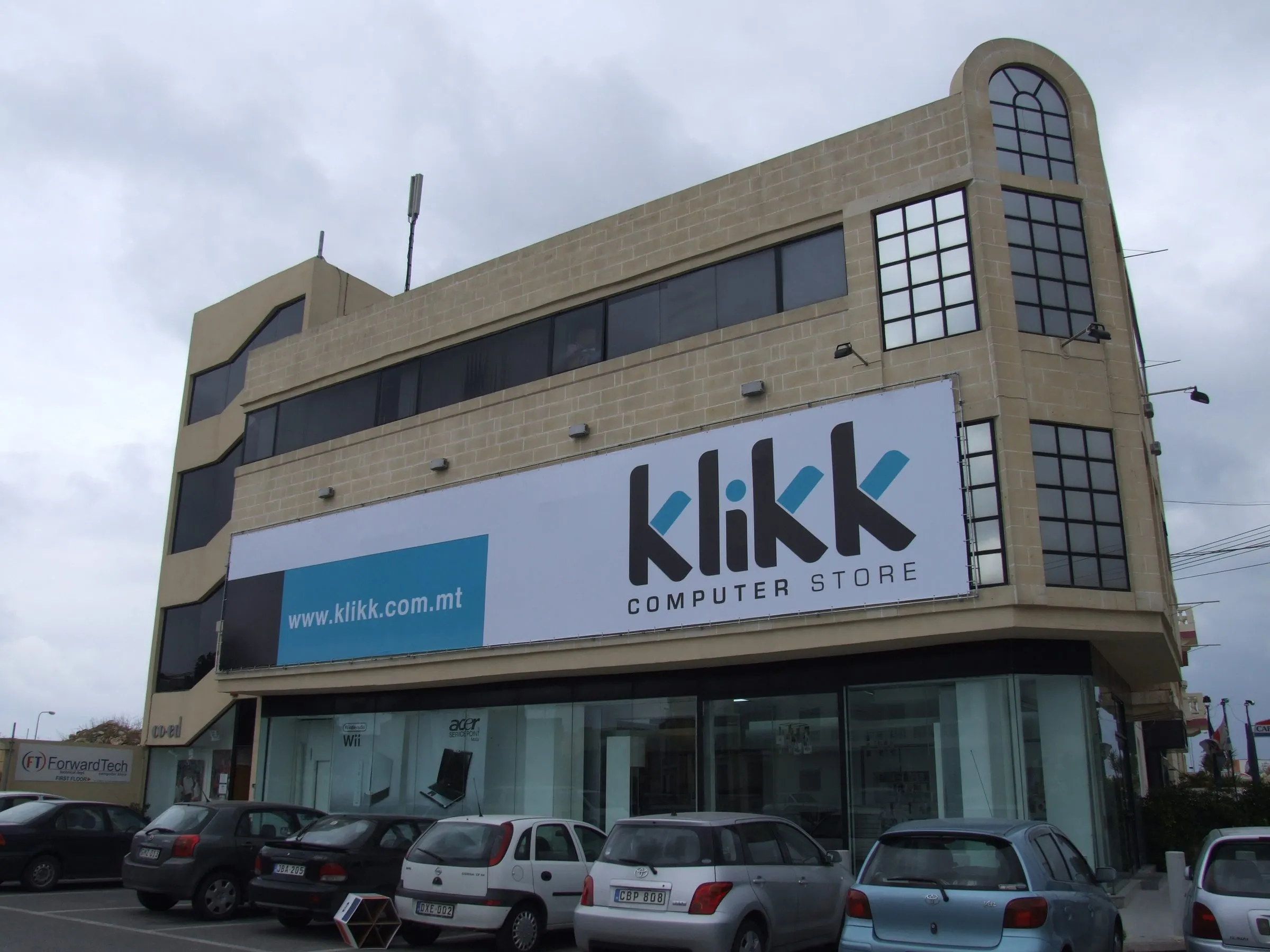 Blue tensioned banner with a store name across the upper elevation of a corner retail building