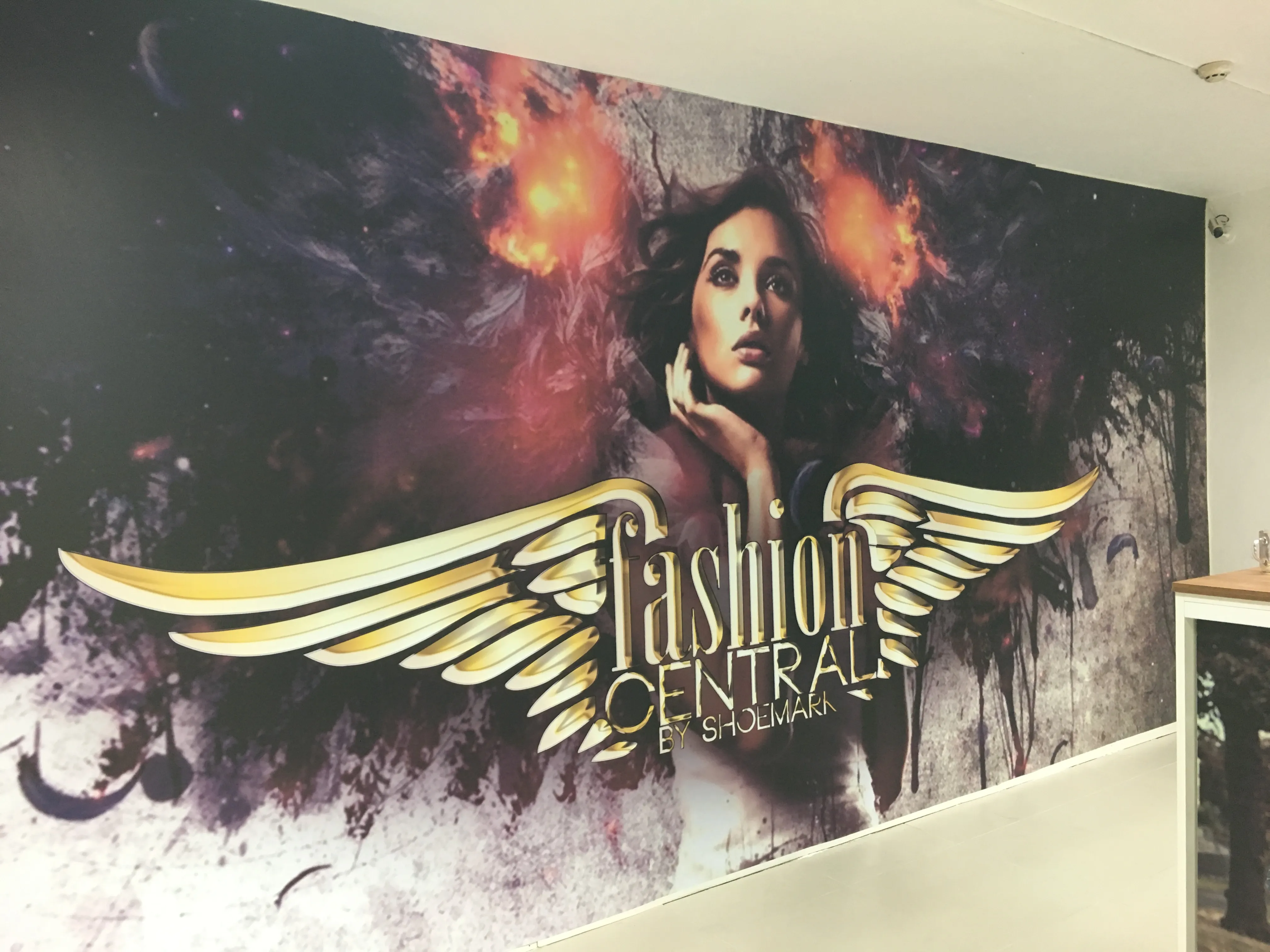 Full-wall photographic mural behind a retail counter, combining a figure, smoke and ember effects and a large gold winged logo device