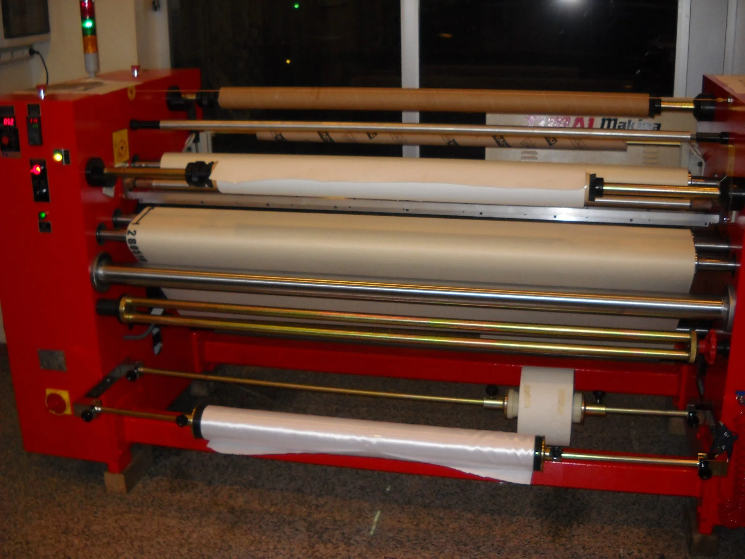 Red wide-format roll laminator loaded with rolls of printed and clear media
