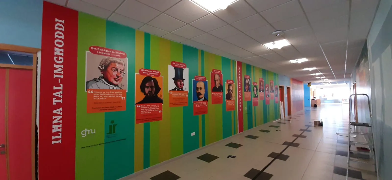 School corridor with a full-length wall graphic in vertical colour bands, carrying portrait panels, quotations and a vertical title running the length of the wall