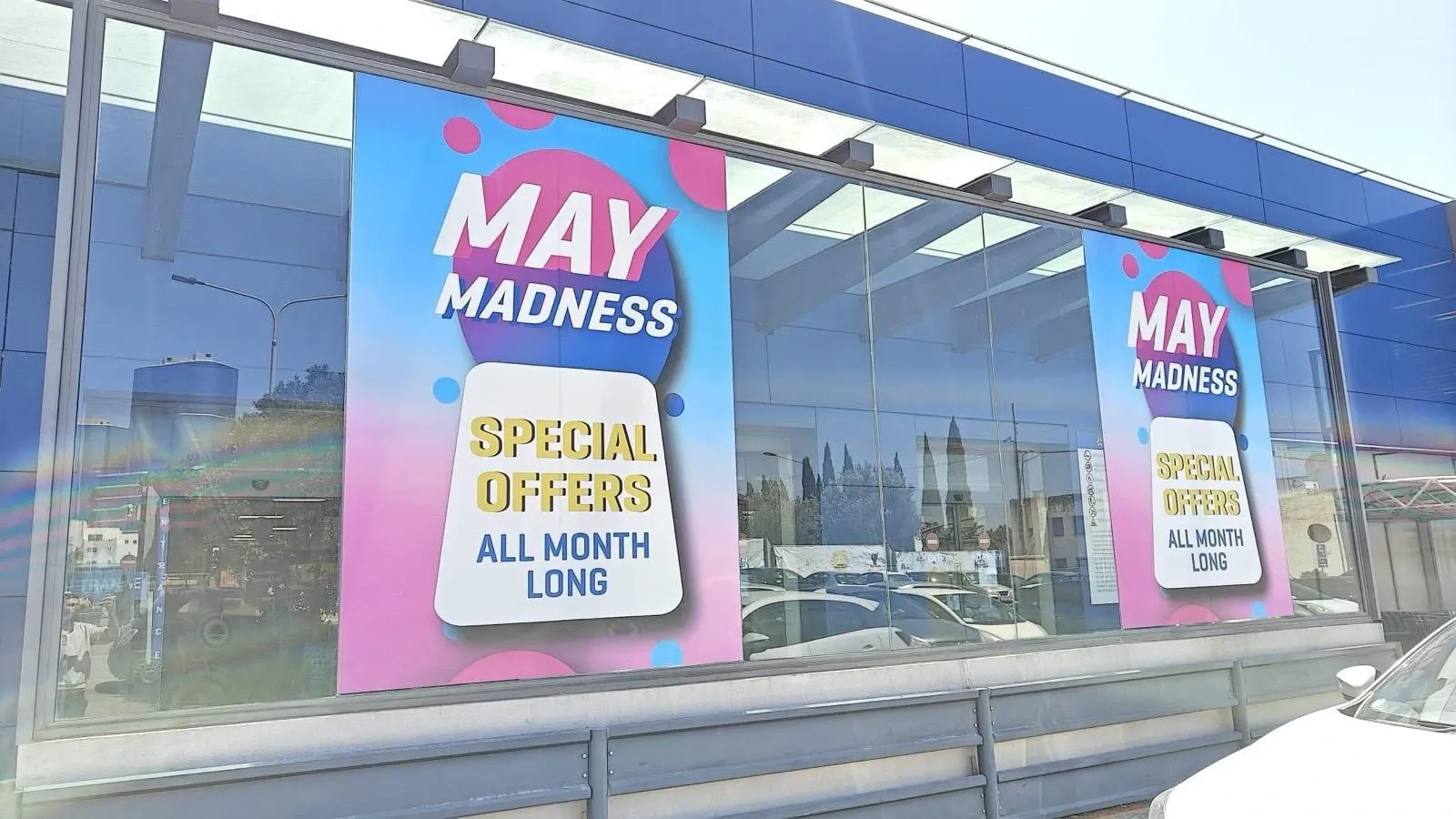 Pink and blue promotional window posters repeated along the glazed frontage of a showroom