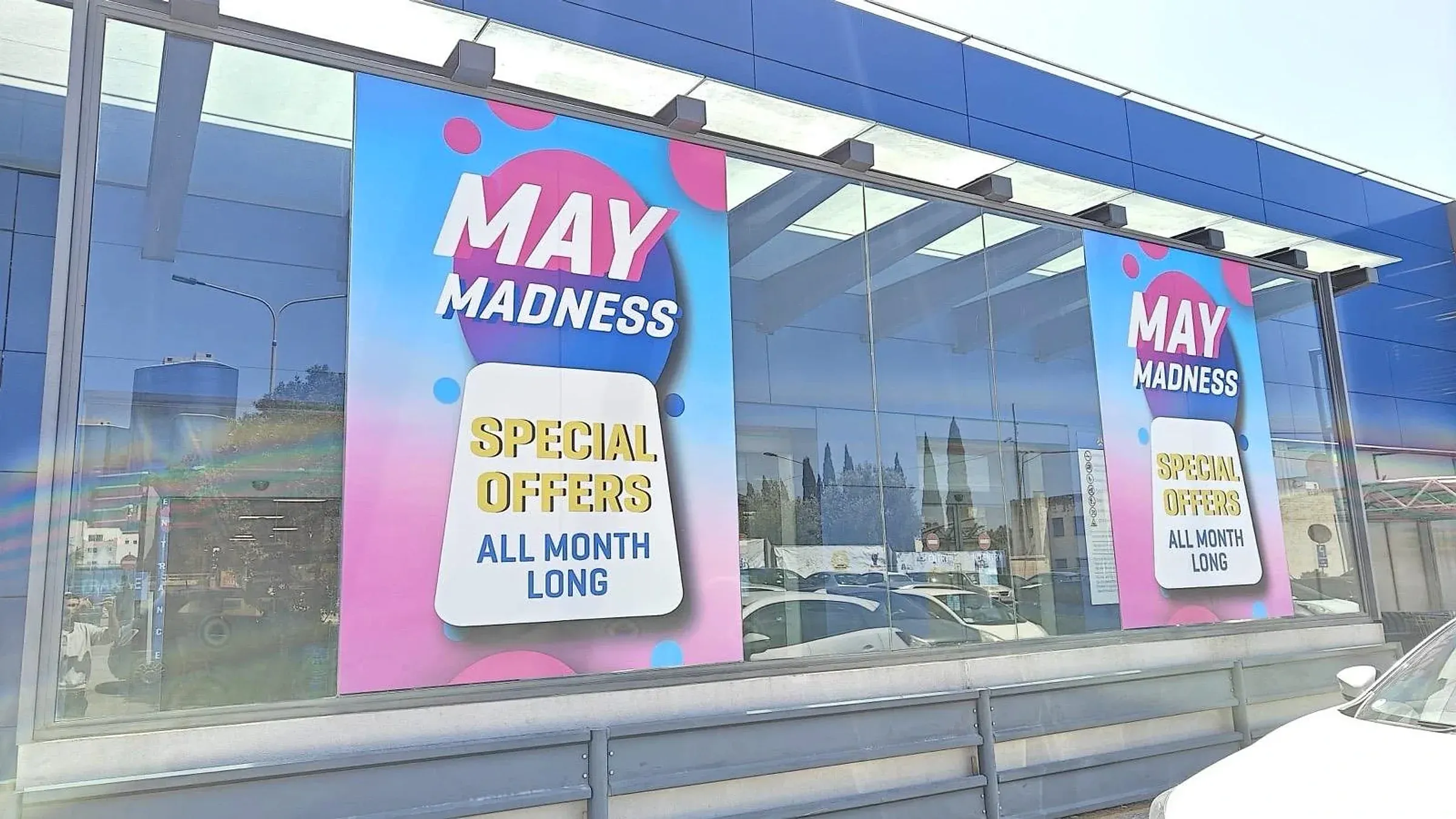 Pink and blue promotional window posters repeated along the glazed frontage of a showroom