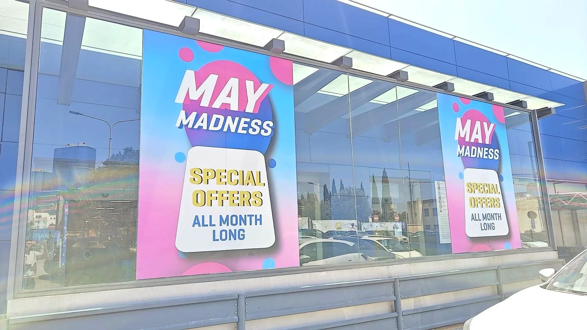 Pink and blue promotional window posters repeated along the glazed frontage of a showroom