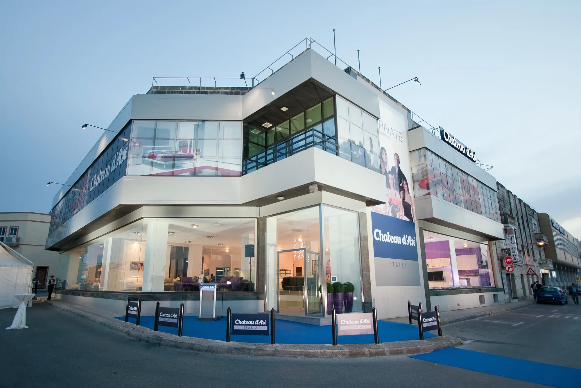 Corner view of a two-storey showroom with facade panels, window graphics and a lit interior