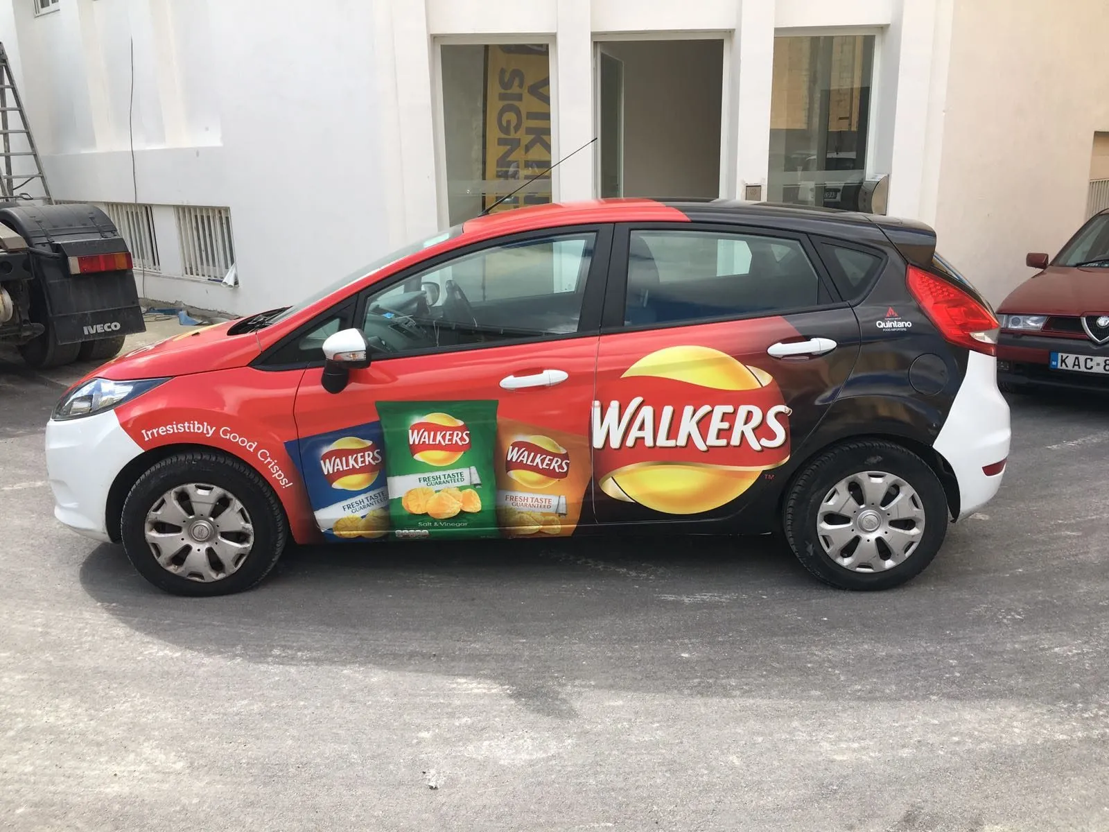 Red and white compact hatchback wrapped with a snack brand graphic, shown side on