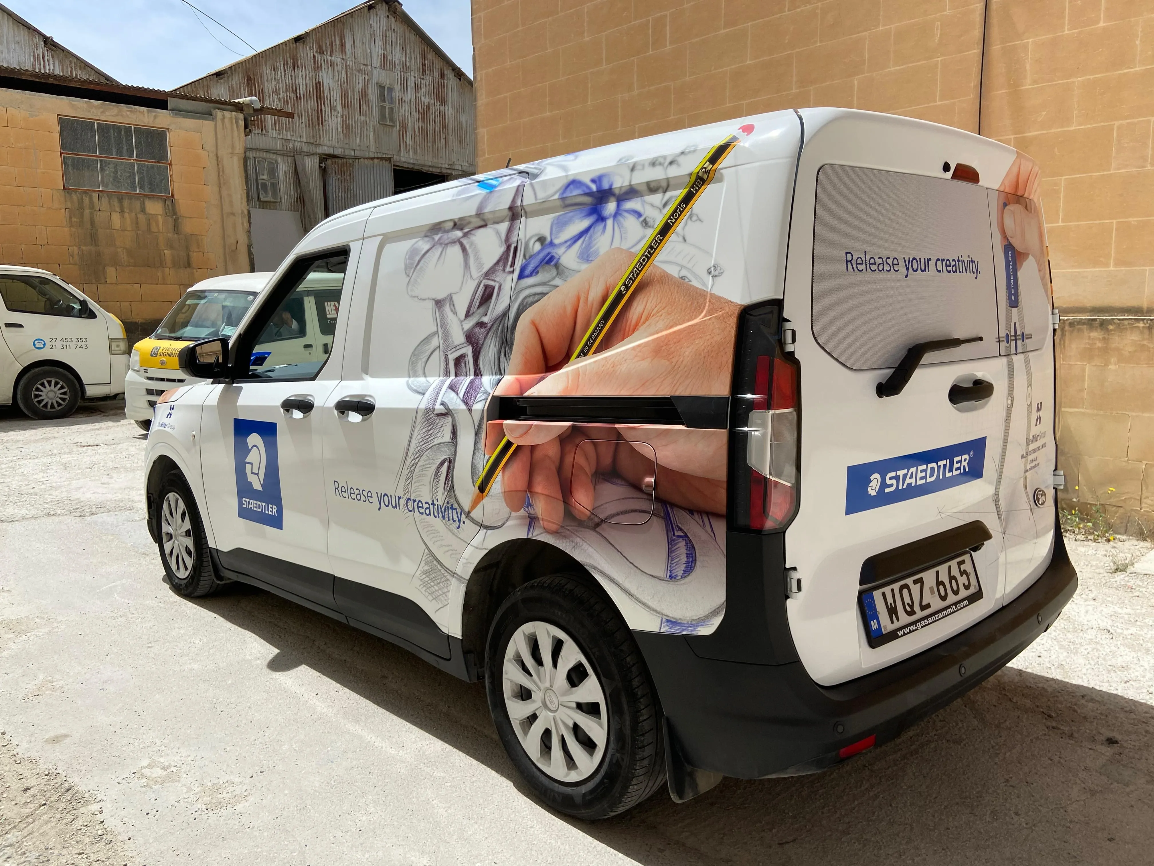 White van wrapped with a large photograph of a hand drawing with a pencil along its side