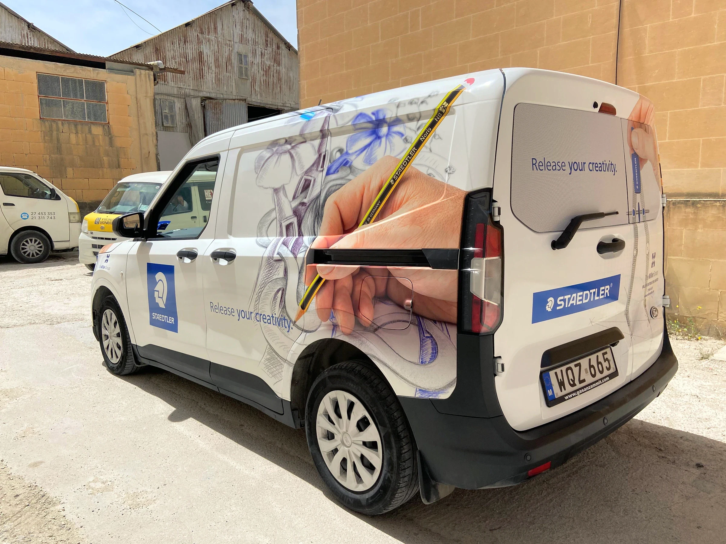 White van wrapped with a large photograph of a hand drawing with a pencil along its side