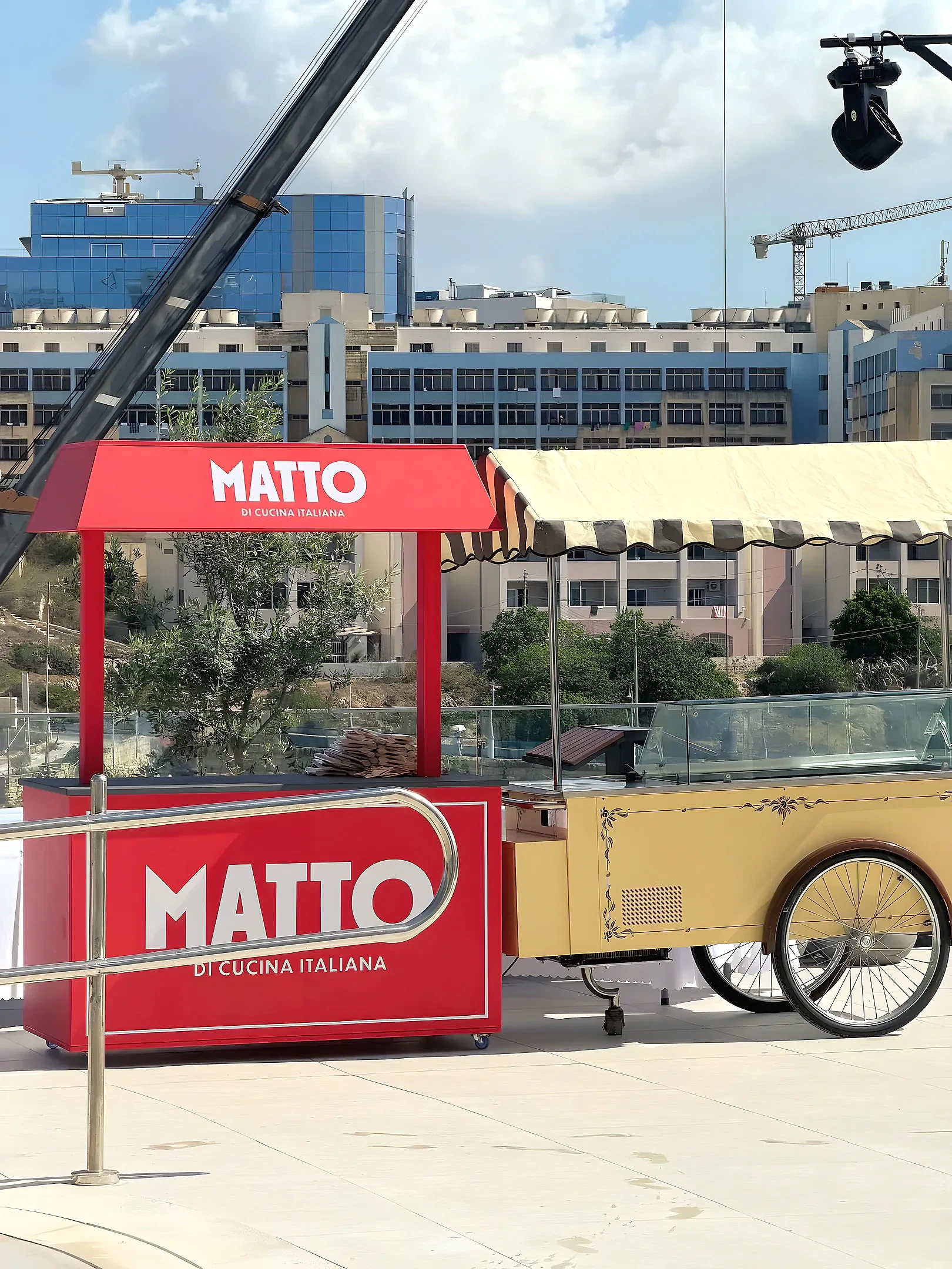 Red branded serving kiosk with a pitched canopy standing on a terrace beside a cream vintage cart
