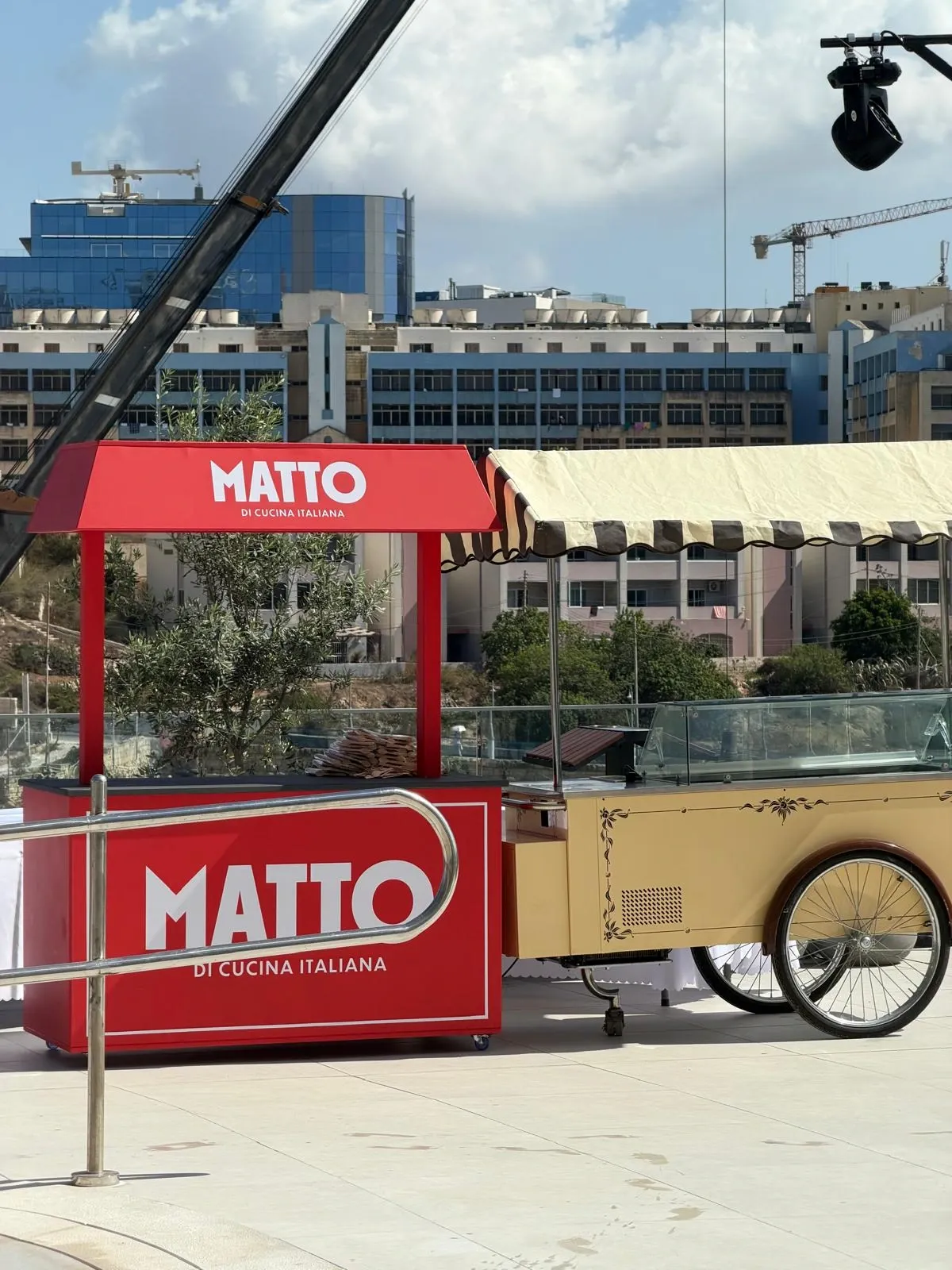 Red branded serving kiosk with a pitched canopy standing on a terrace beside a cream vintage cart