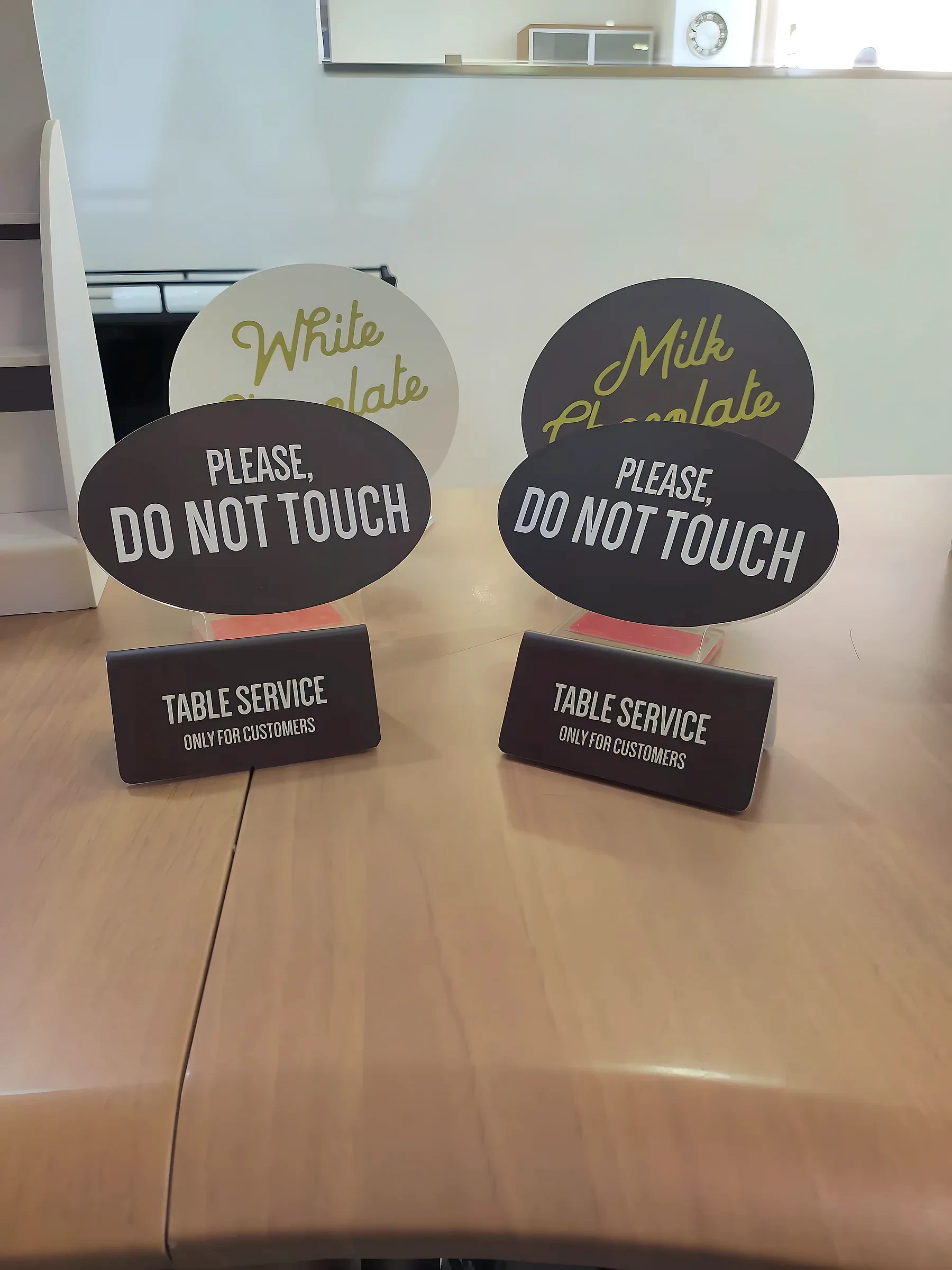 Two oval tabletop signs reading please do not touch on printed table service bases
