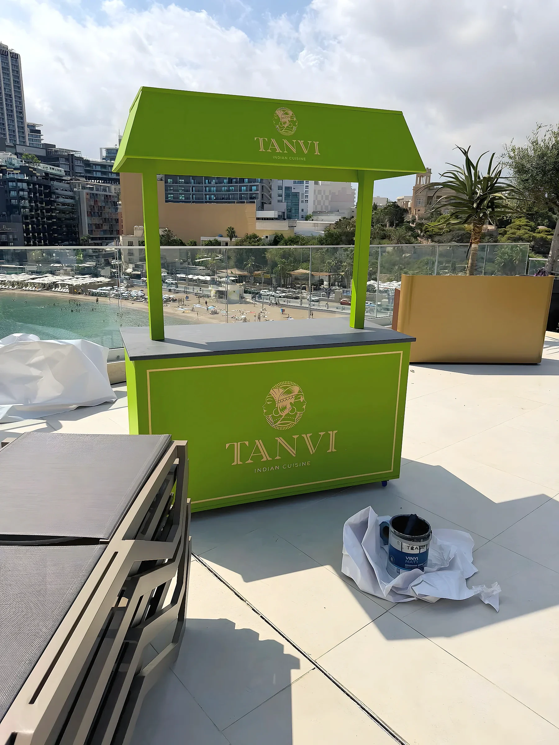 Green branded kiosk with a canopy standing on a hotel terrace overlooking a bay