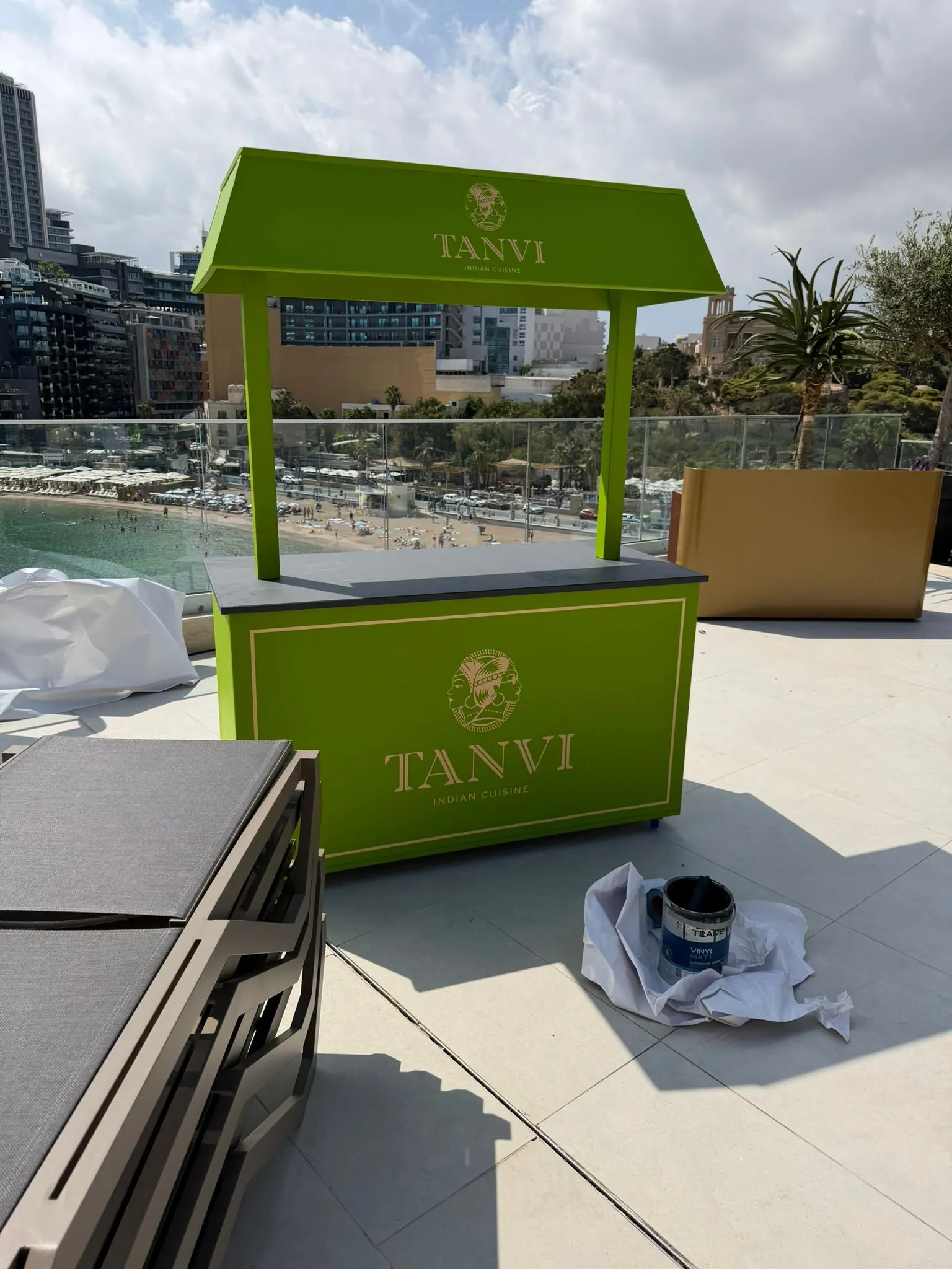 Green branded kiosk with a canopy standing on a hotel terrace overlooking a bay