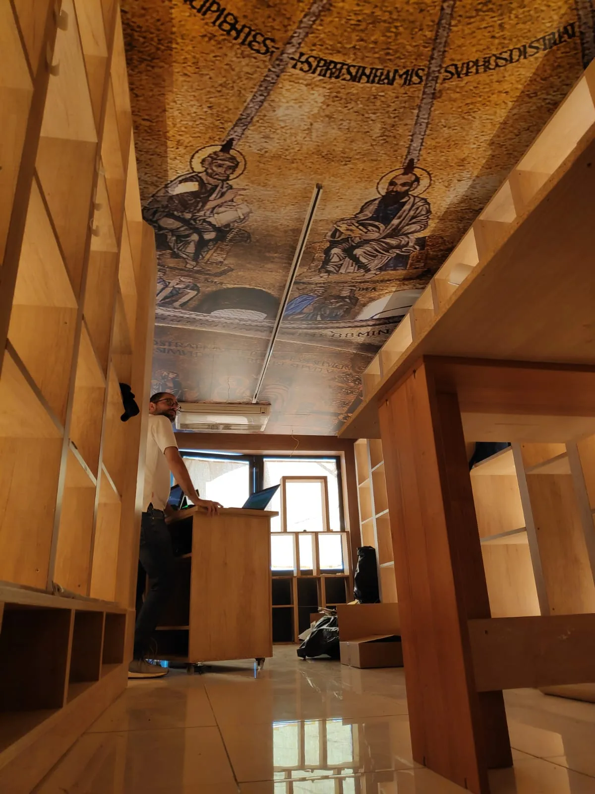 The same ceiling seen along the room during fit-out, with the printed vault running above unfinished timber joinery and a worker at a counter