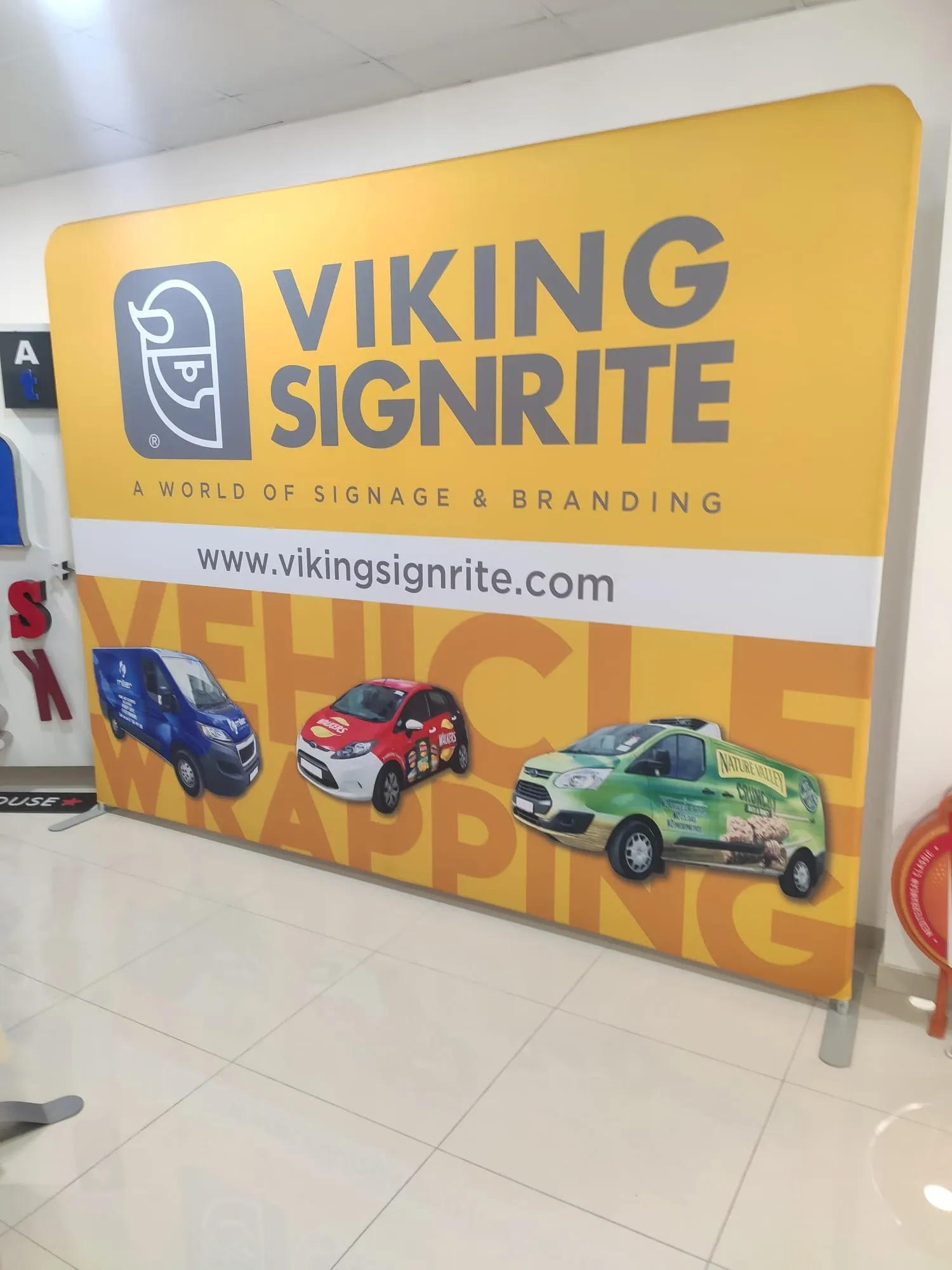 Yellow Viking Signrite fabric display wall showing three wrapped vehicles, standing in the workshop